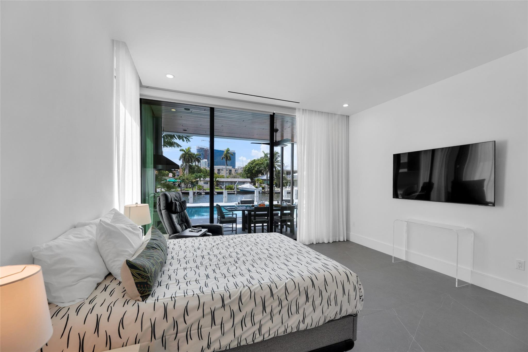 Furnished bedroom overlooking a pool and canal through floor-to-ceiling glass doors.