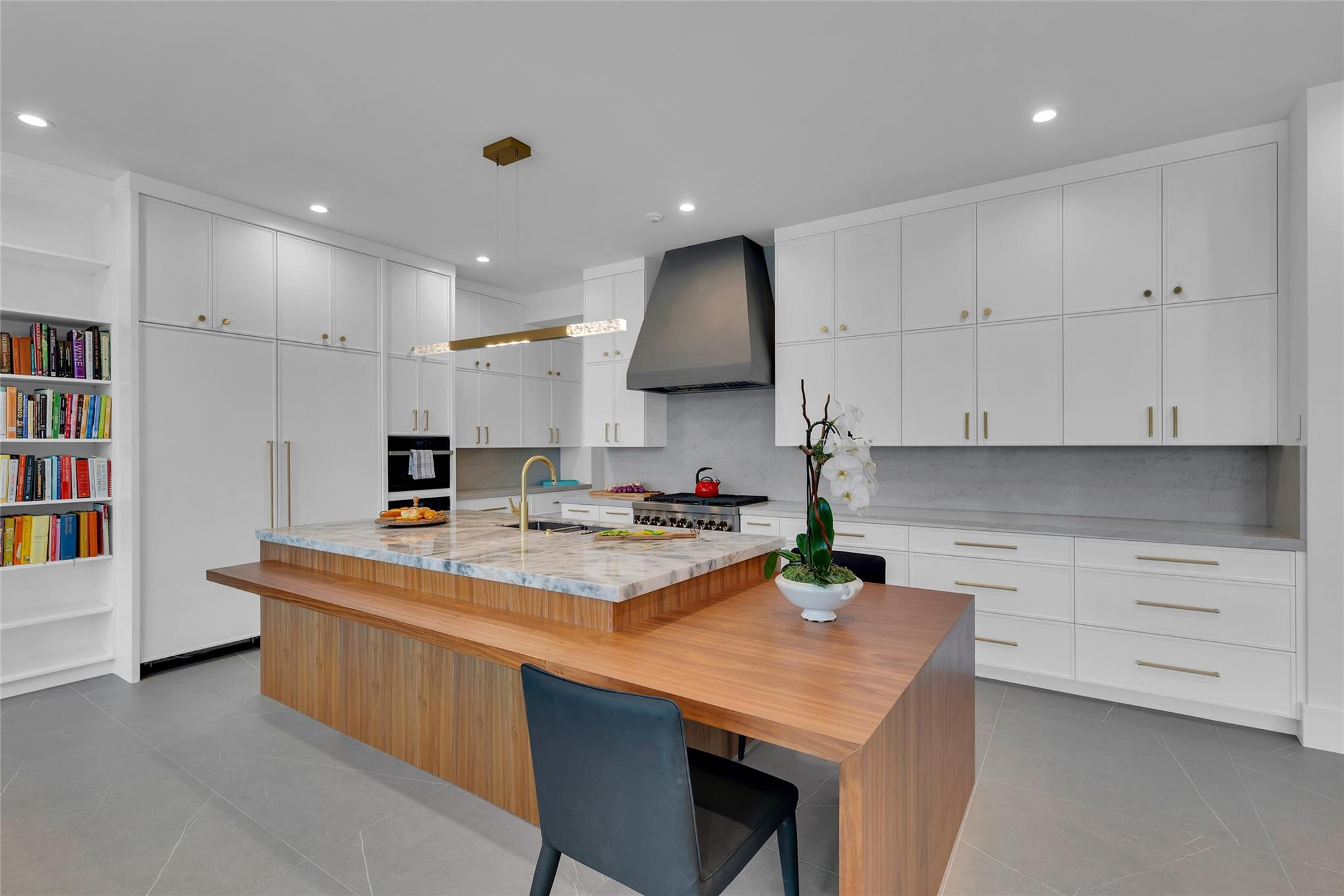 Modern white kitchen with a marble island and attached walnut dining counter.