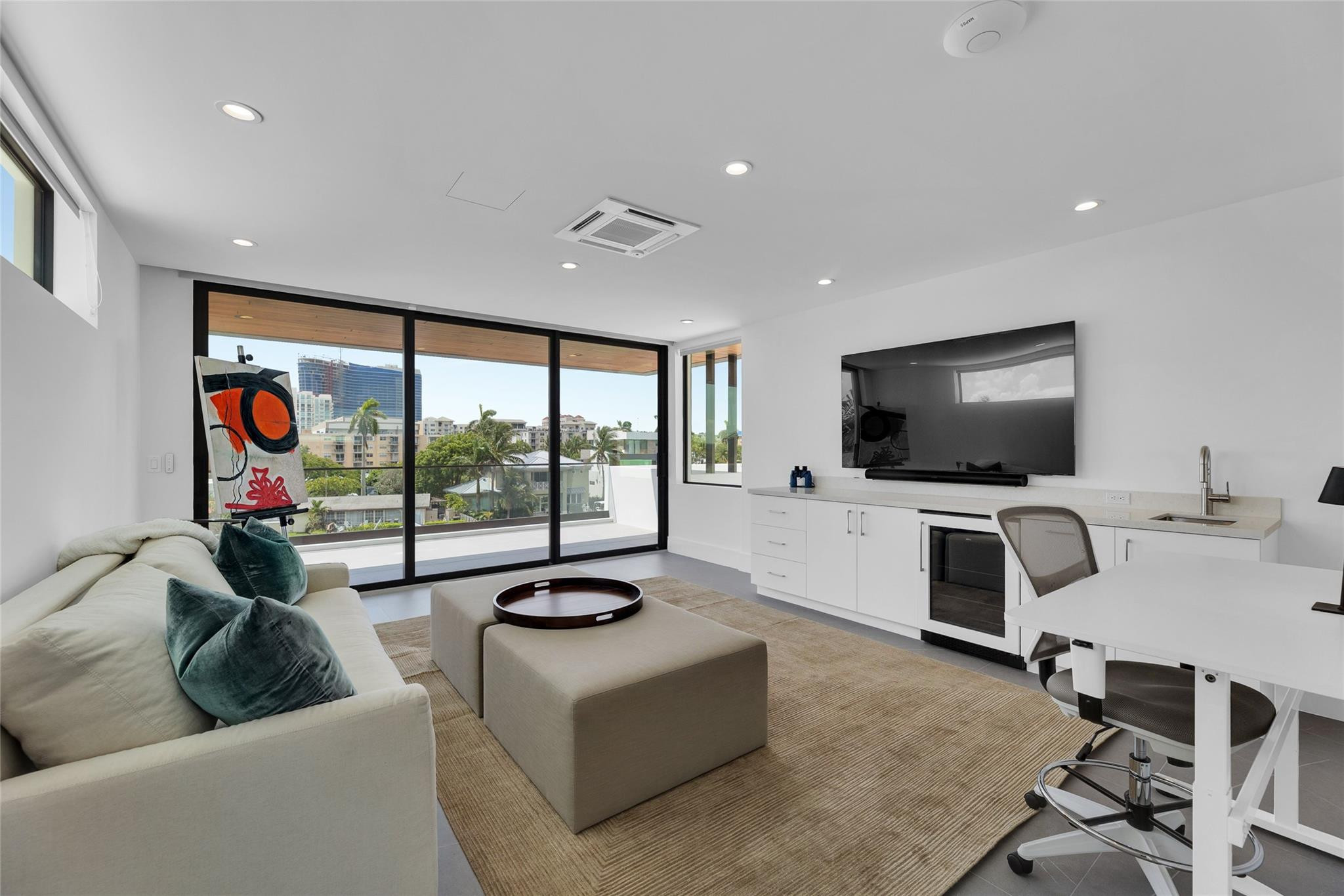 Furnished living room with floor-to-ceiling glass doors, palm trees, and city buildings outside.