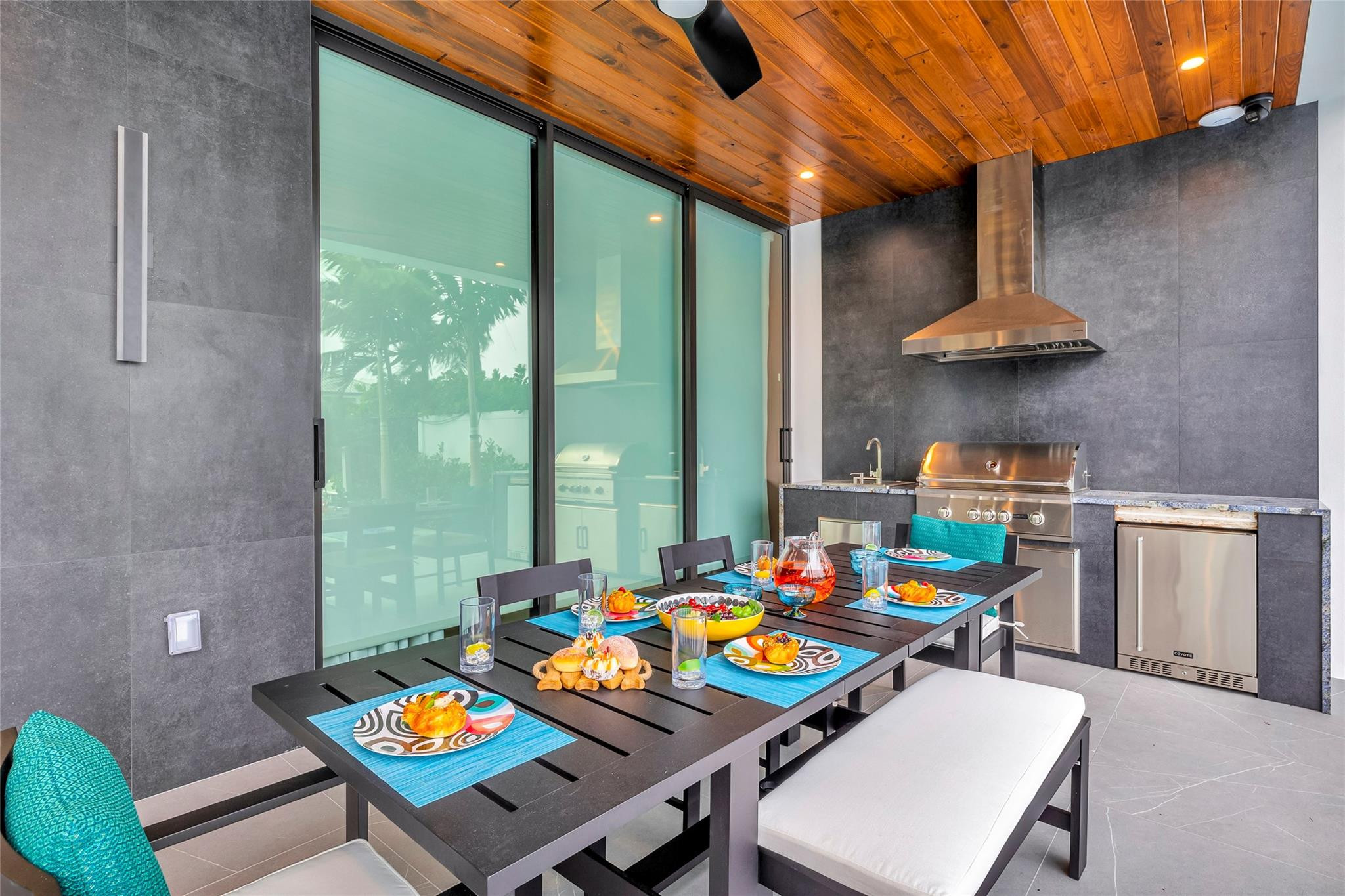 Covered outdoor dining area with a wood ceiling, set table, and built-in stainless steel grill.