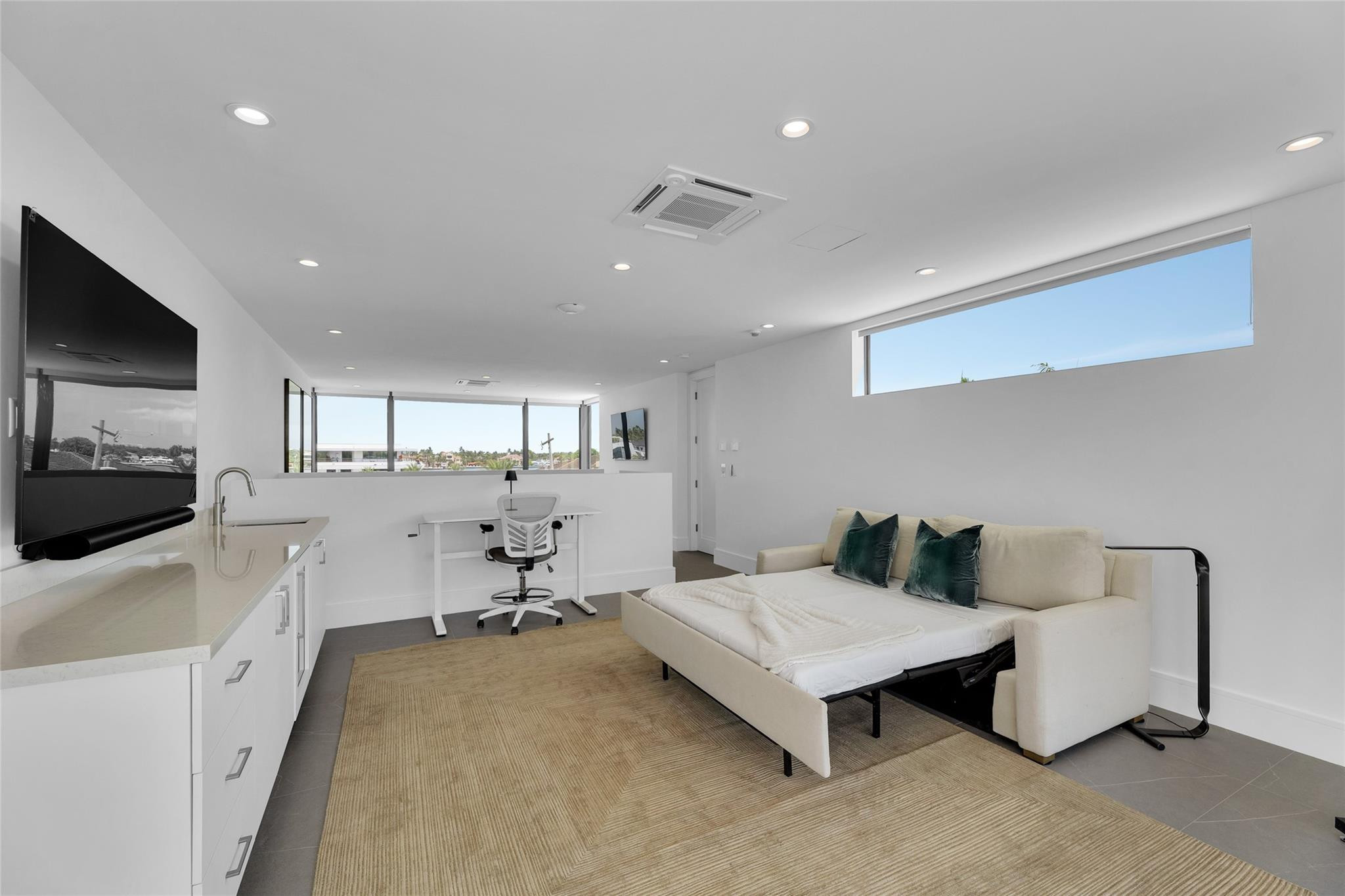 Modern living room with a cream sofa bed, built-in cabinets, desk, and broad windows.