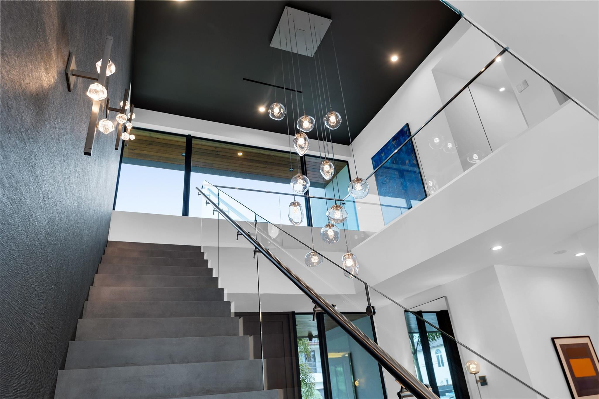 Modern staircase with glass railings, dramatic pendant lights, and a double-height ceiling
