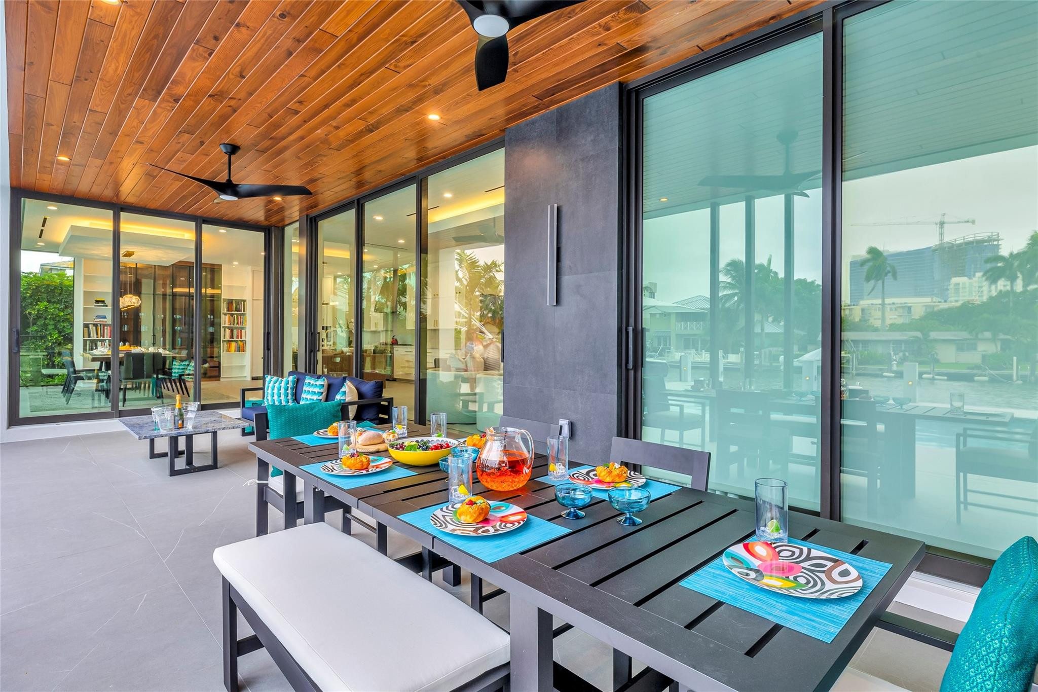 Covered patio dining area with a wood ceiling, turquoise seating, and canal views through glass doors.