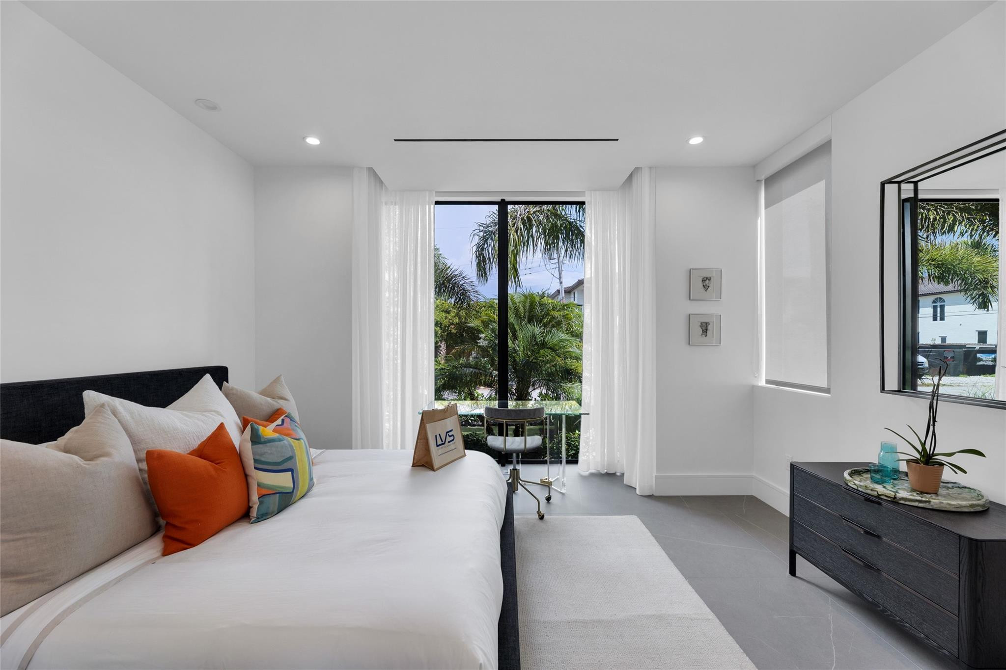 Modern bedroom with colorful pillows and glass doors overlooking palm trees.