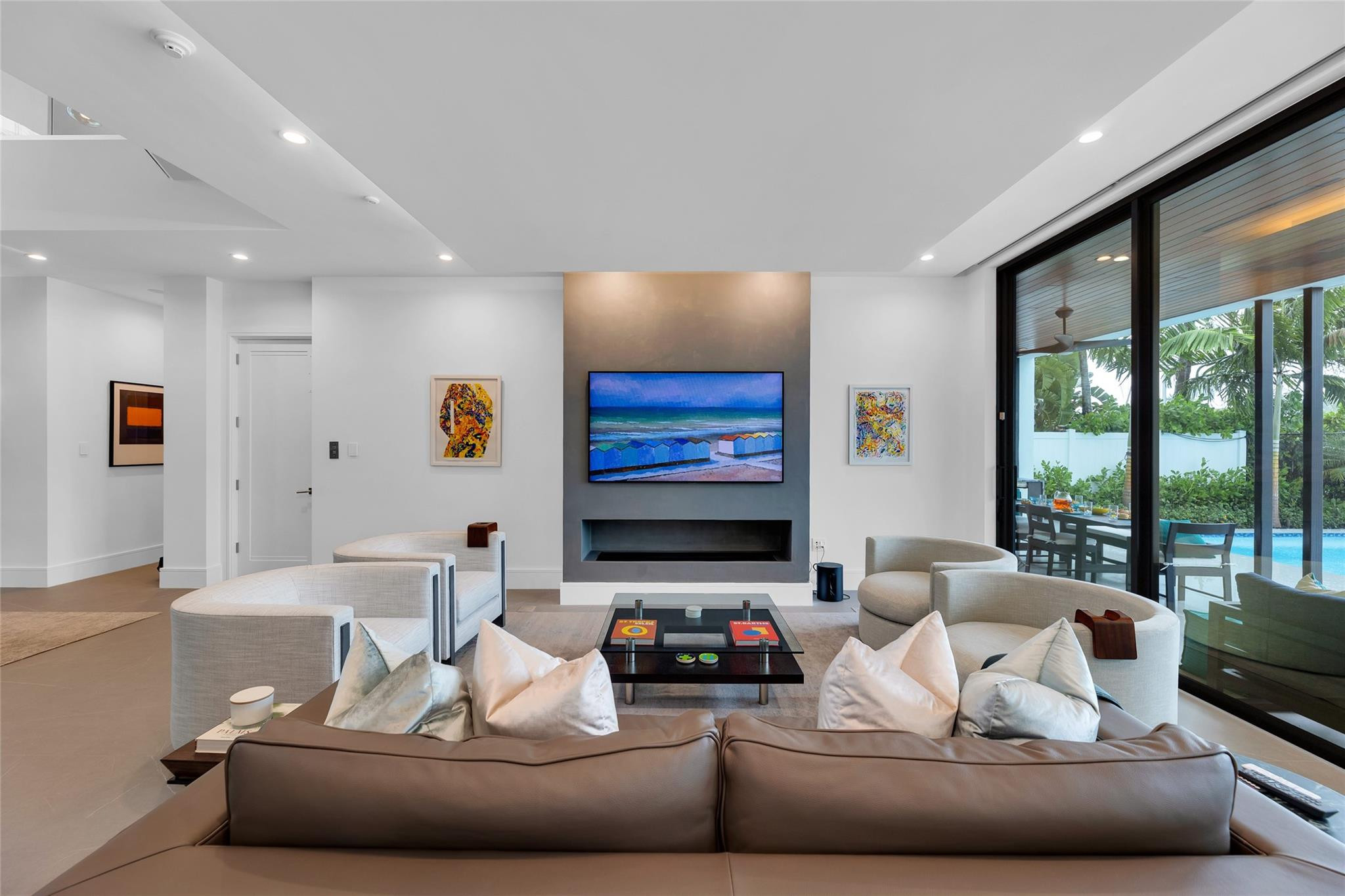 Modern living room with a brown sectional, fireplace wall, and glass doors overlooking a poolside patio.