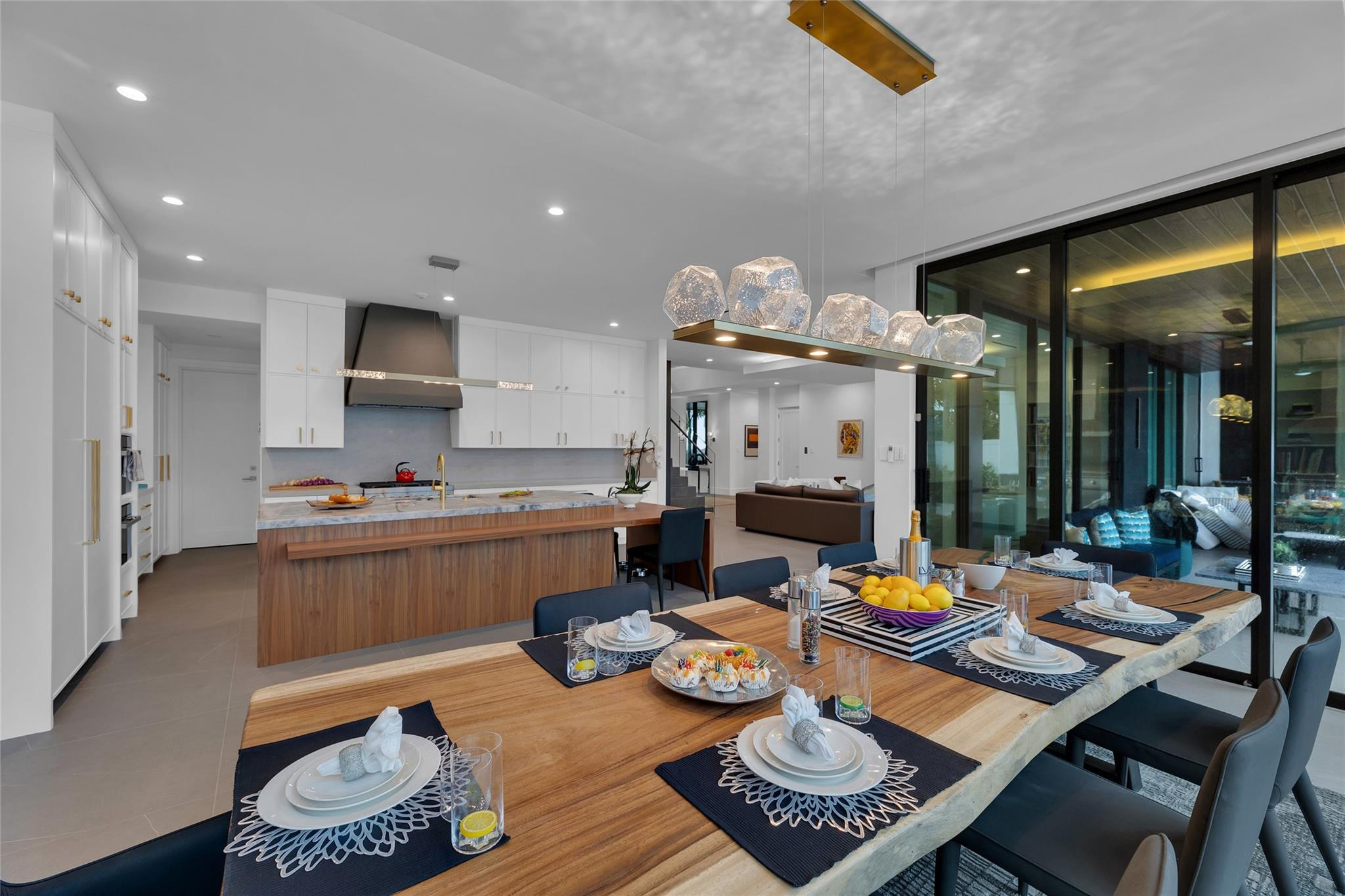 Open-plan kitchen and dining area with a wood island, set dining table, and black-framed glass doors.