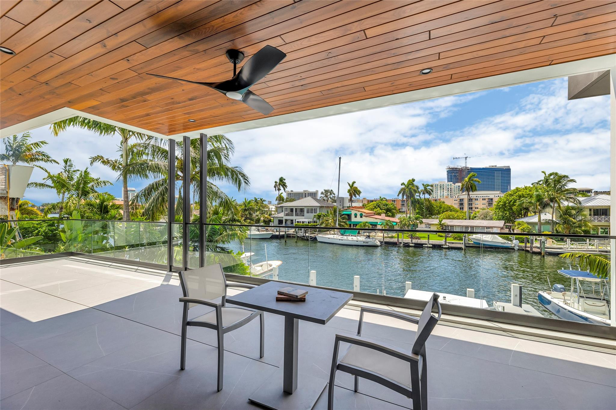 Covered patio overlooking a boat-lined canal, with a wood ceiling and glass railing.
