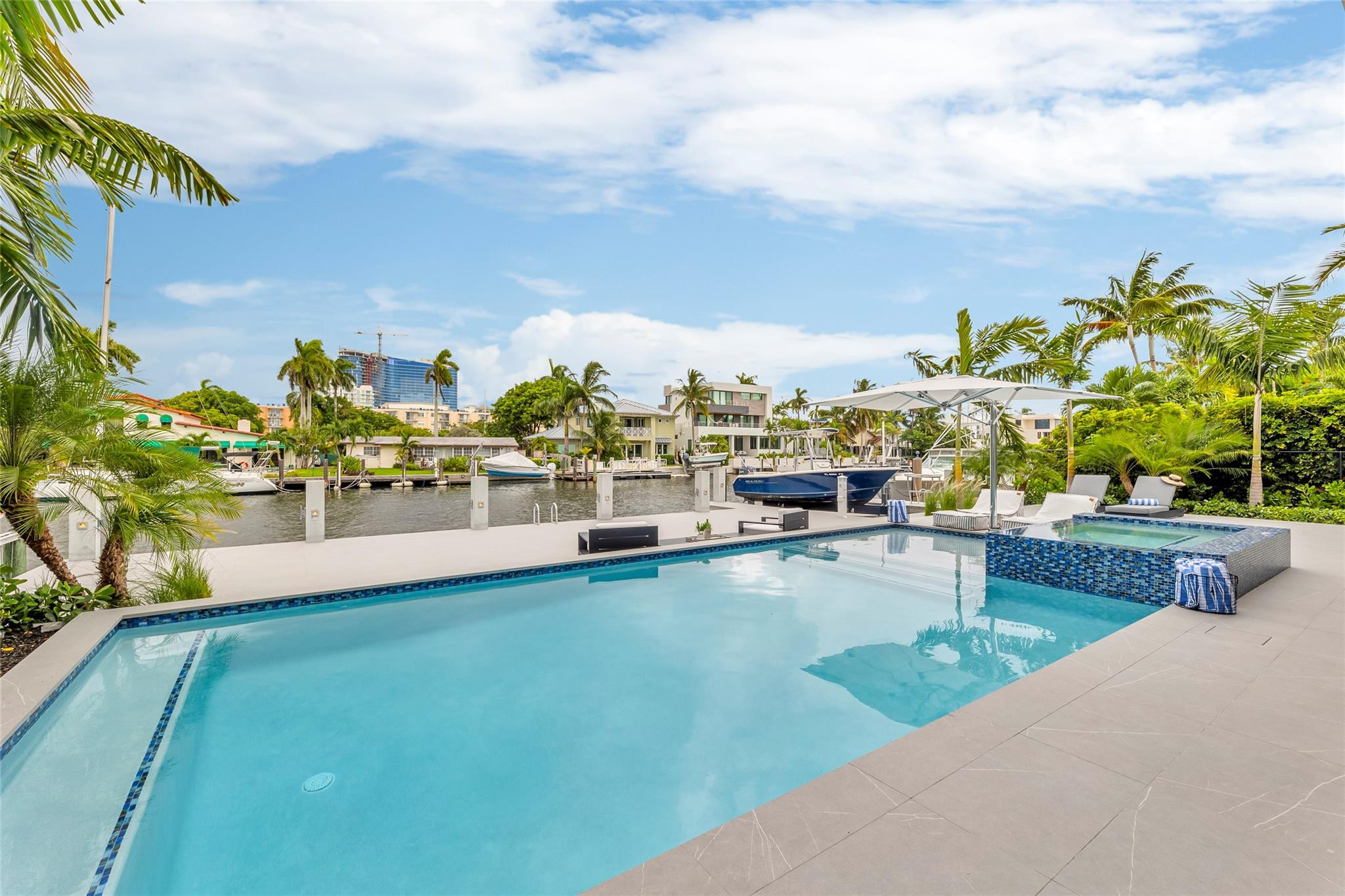 Backyard pool and raised spa beside a palm-lined canal with boats.