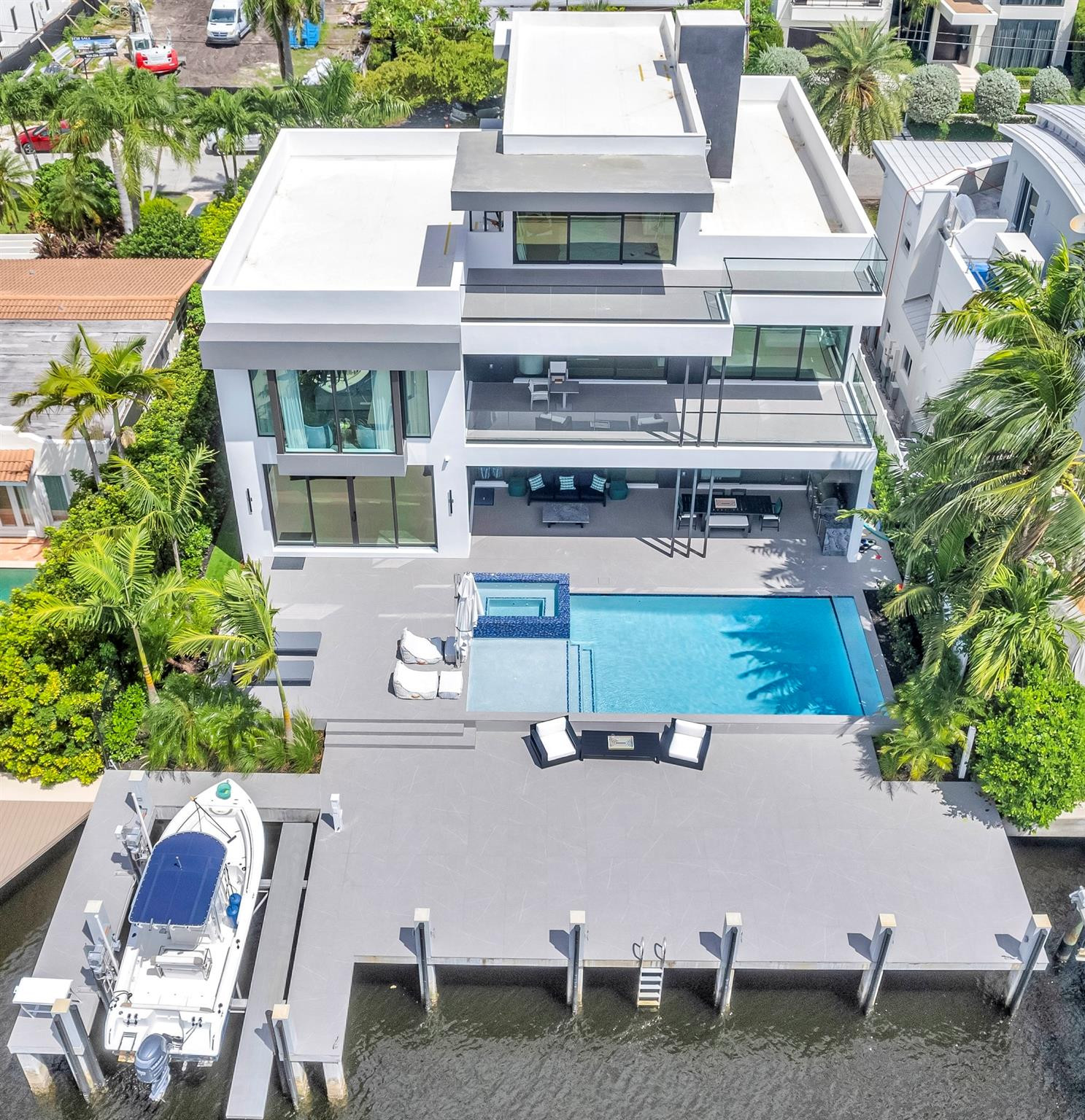 Aerial view of a modern waterfront home with a pool, glass balconies, and a docked boat.