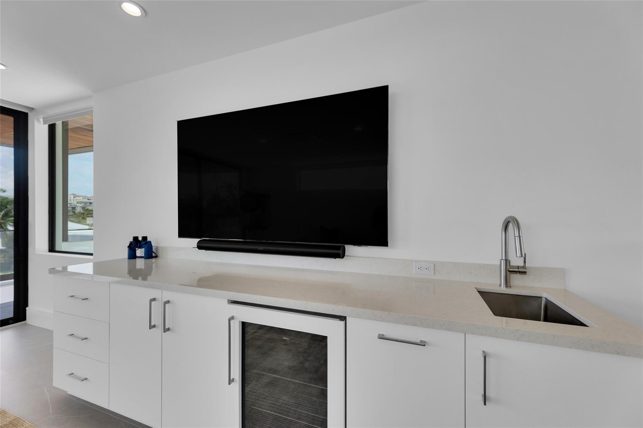 Modern wet bar with a wall-mounted television, sink, and under-counter beverage refrigerator.