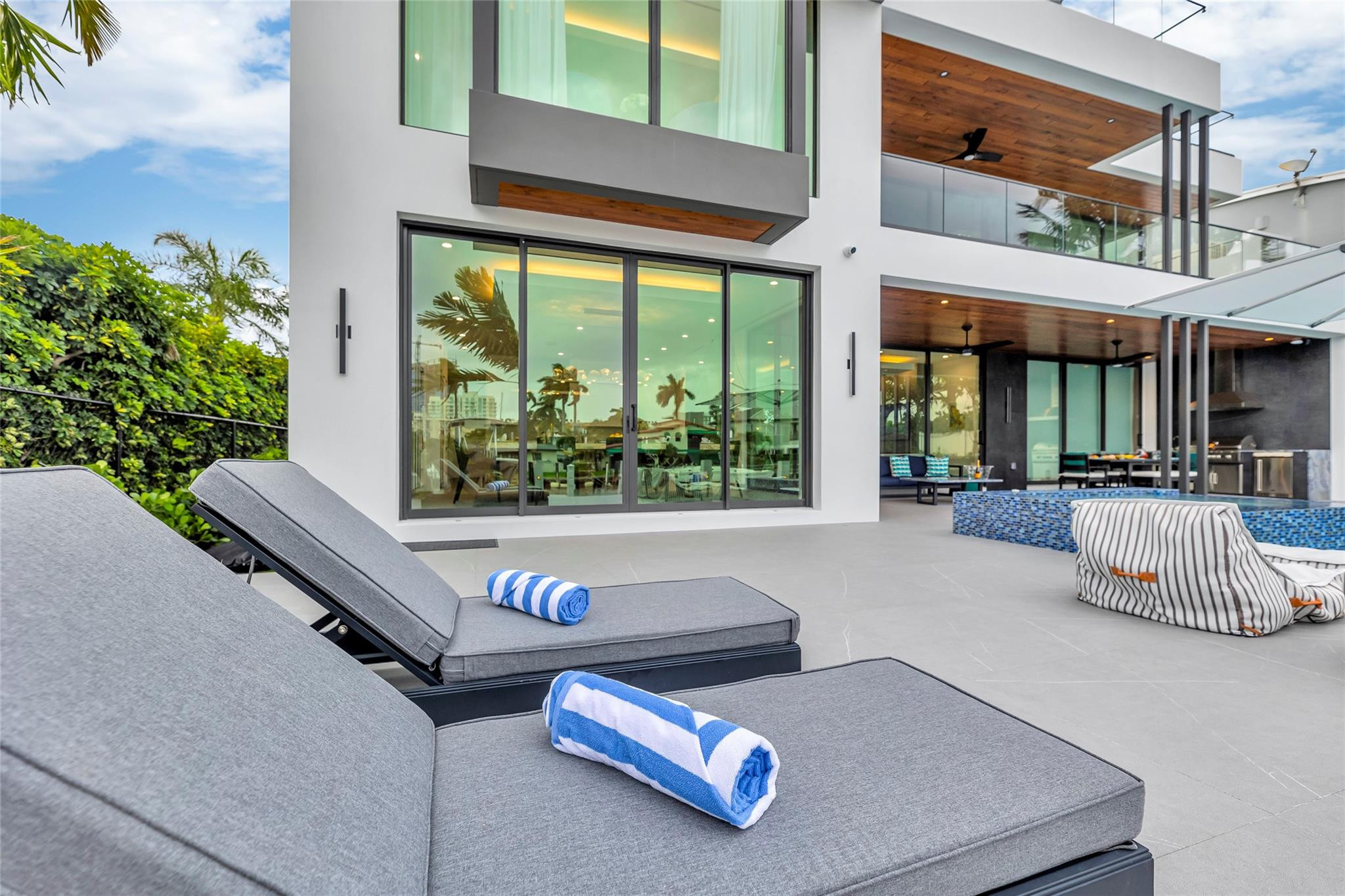 Modern home’s pool deck with blue-tiled pool, gray chaise lounges, and covered outdoor dining area.