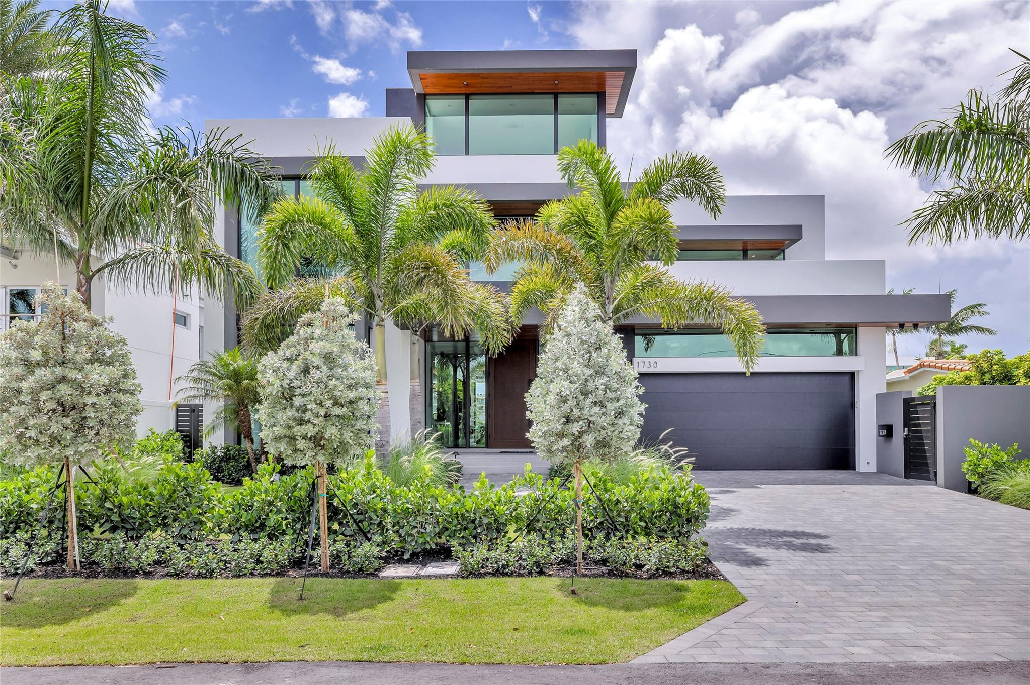 Modern two-story home with tropical landscaping, a dark garage door, and the number 1730 above it.