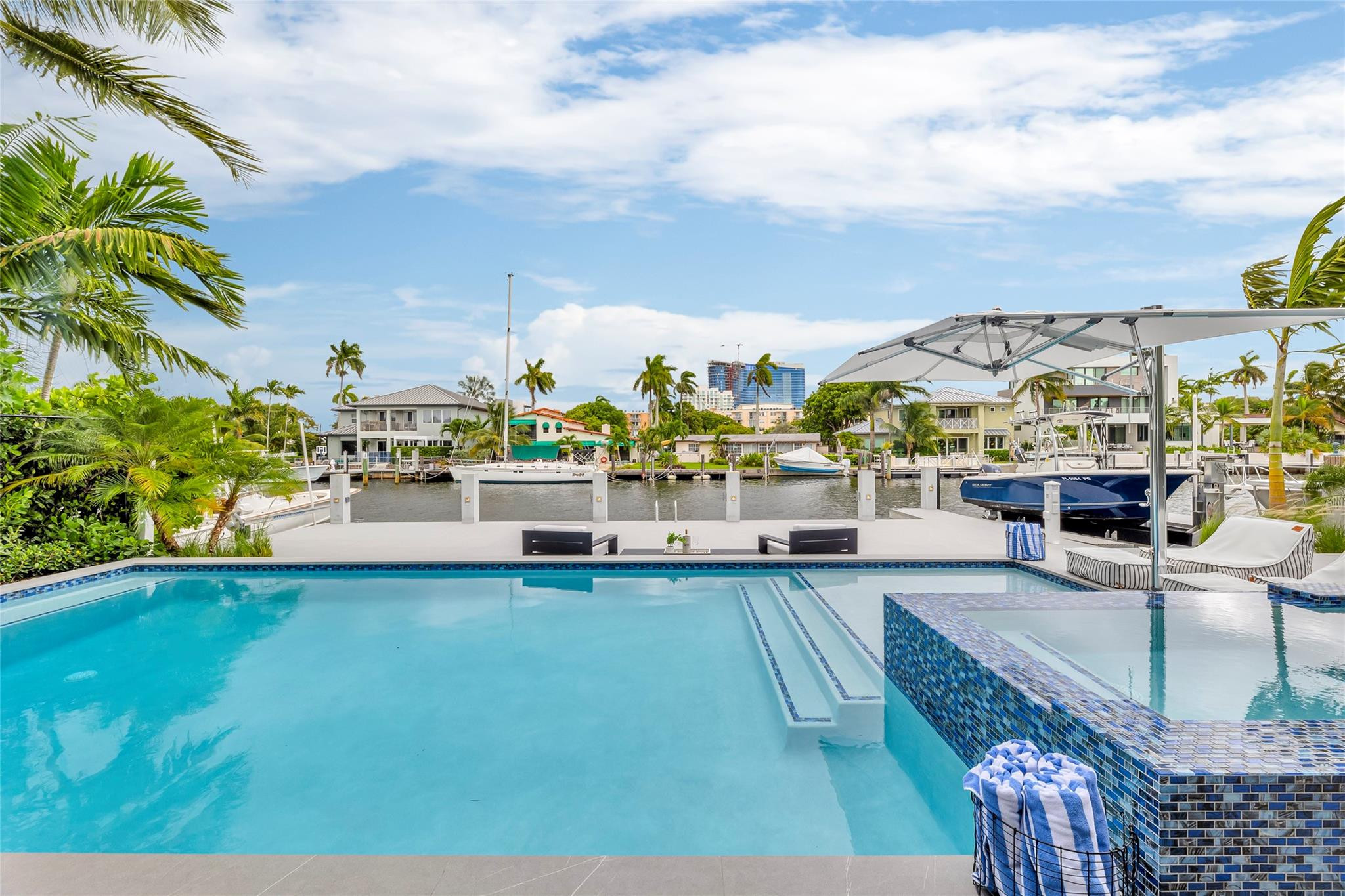Waterfront pool and raised tiled spa beside a canal, with boats and palm-lined homes beyond.