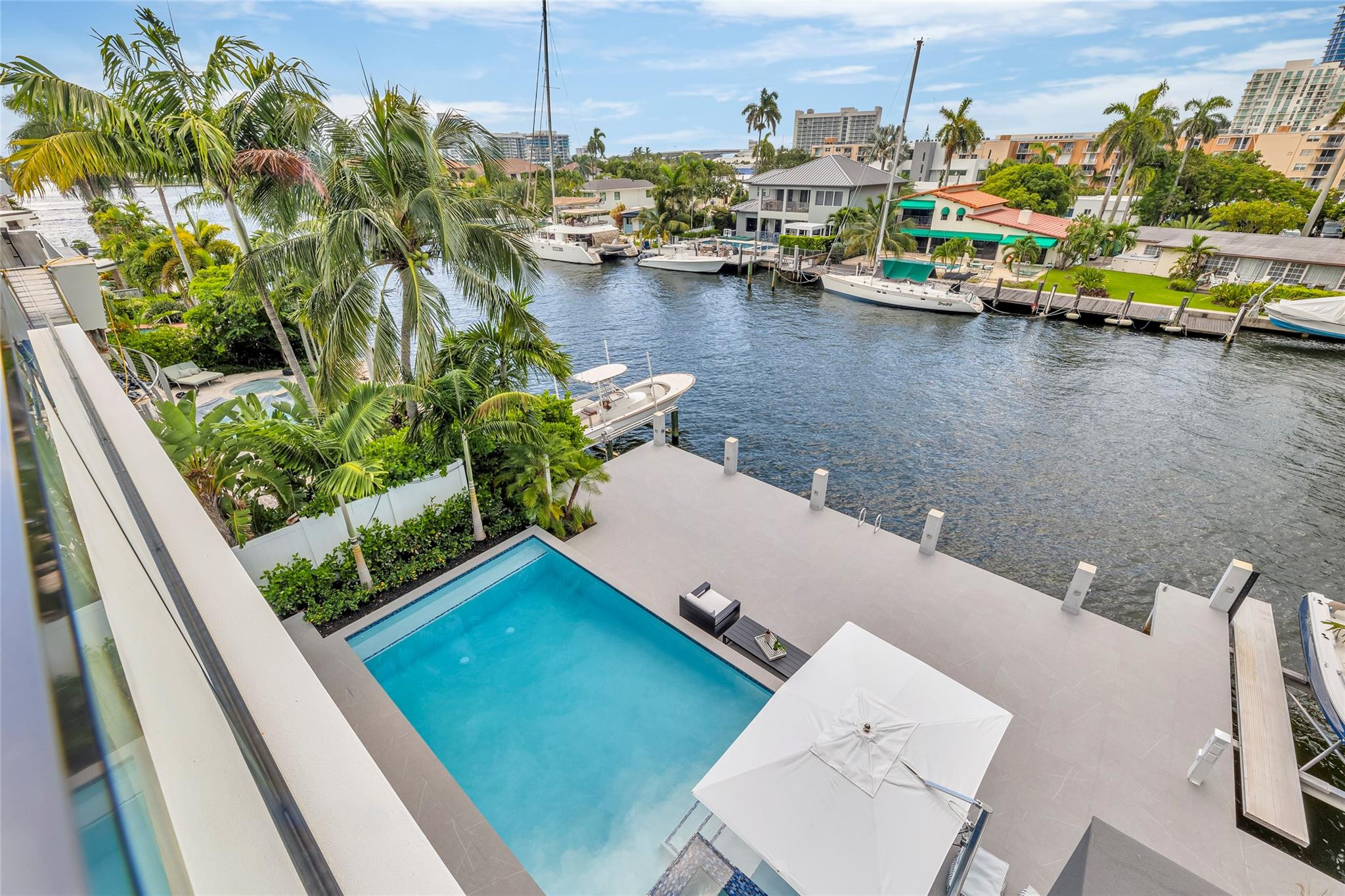 Waterfront backyard with a turquoise pool, spacious canal-side dock, moored boats, and tropical palms.