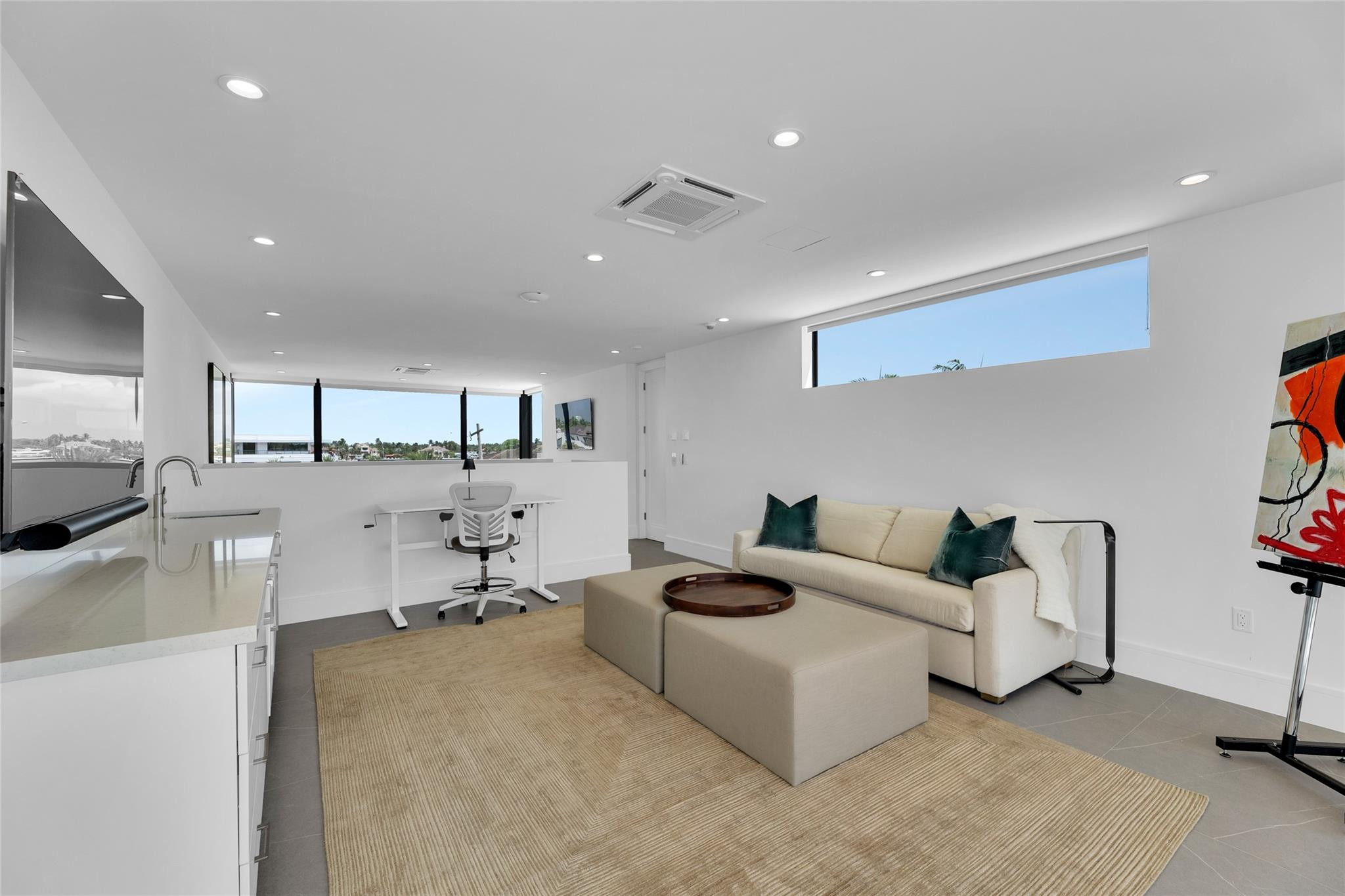 Modern home office and sitting area with a cream sofa, ottoman, and large windows.