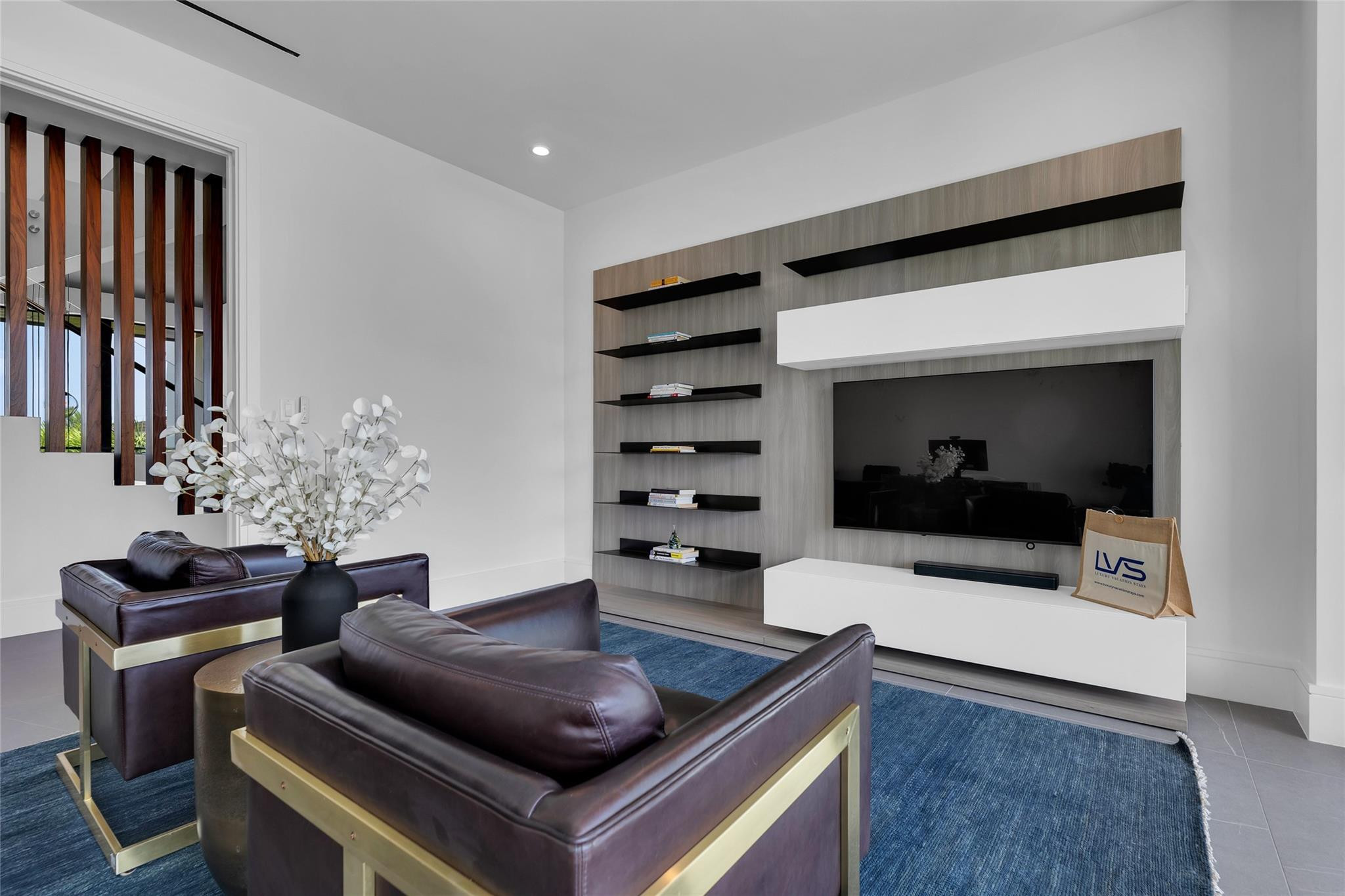 Furnished living room with leather armchairs, blue rug, and built-in media wall.