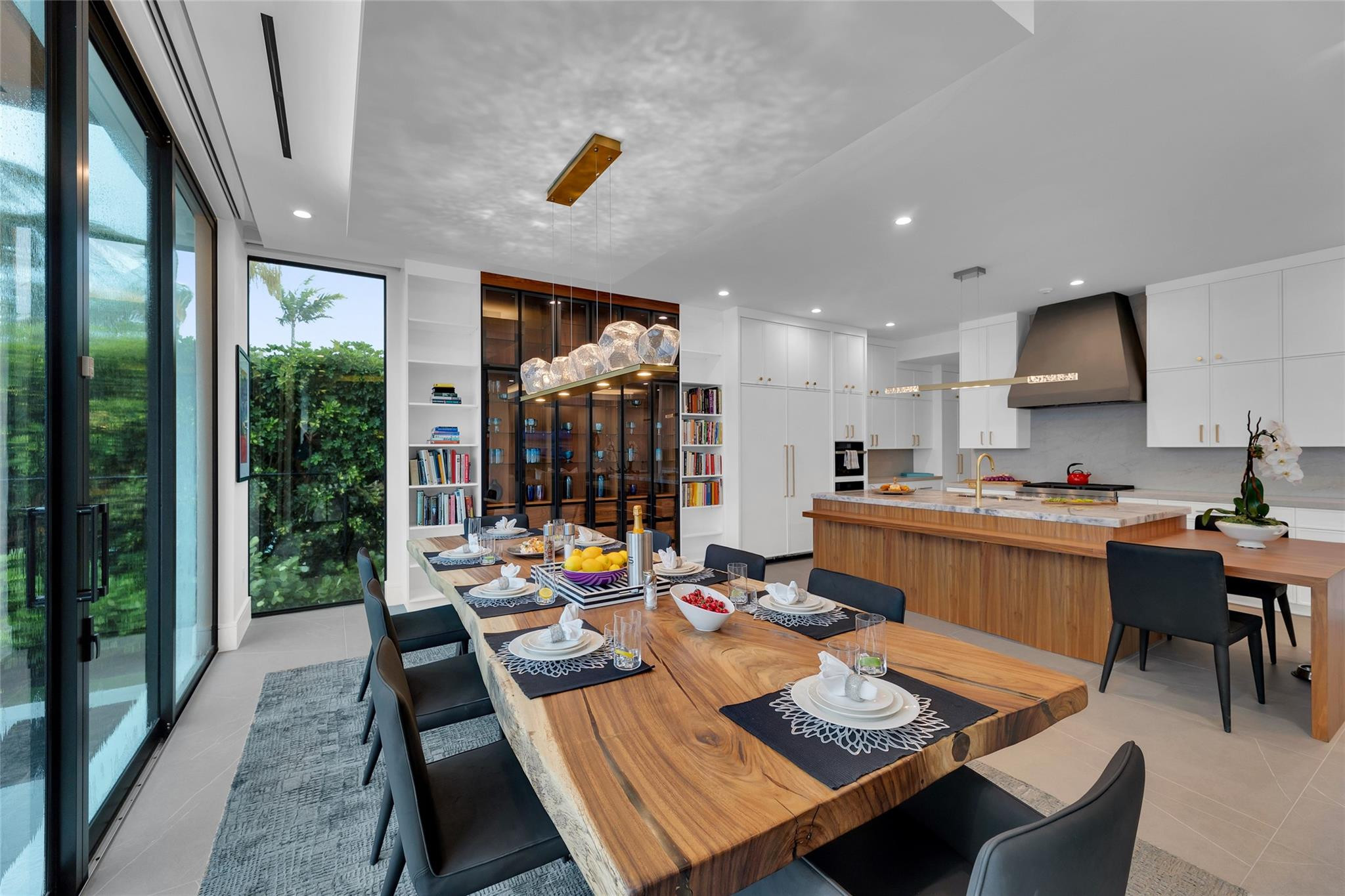 Modern kitchen and dining room with a live-edge table, wood island, and glass doors to a leafy garden.
