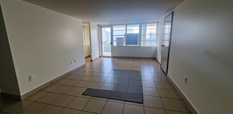 Empty living room with beige tile floors, a dark mat, and large windows.
