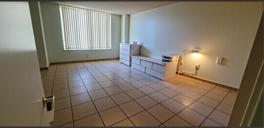 Empty condo room with tiled floors, vertical blinds, and built-in white drawers.