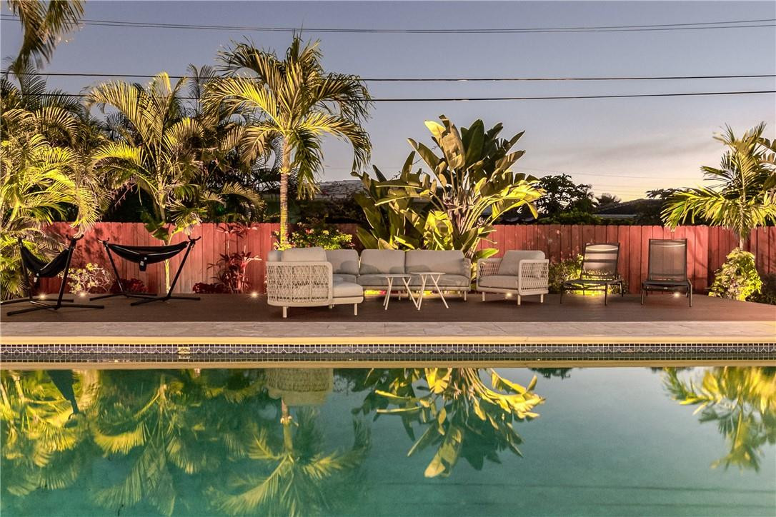 Swimming pool beside a tropical patio with lounge seating, a hammock, and palm trees.