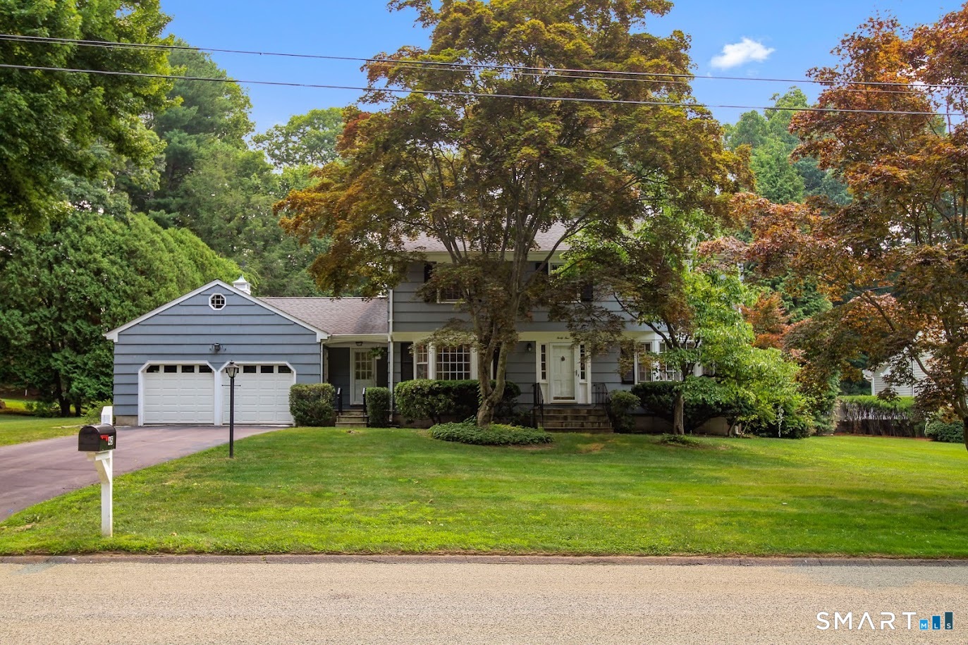 Gray two-story house with an attached garage, broad lawn, and mature autumn trees.