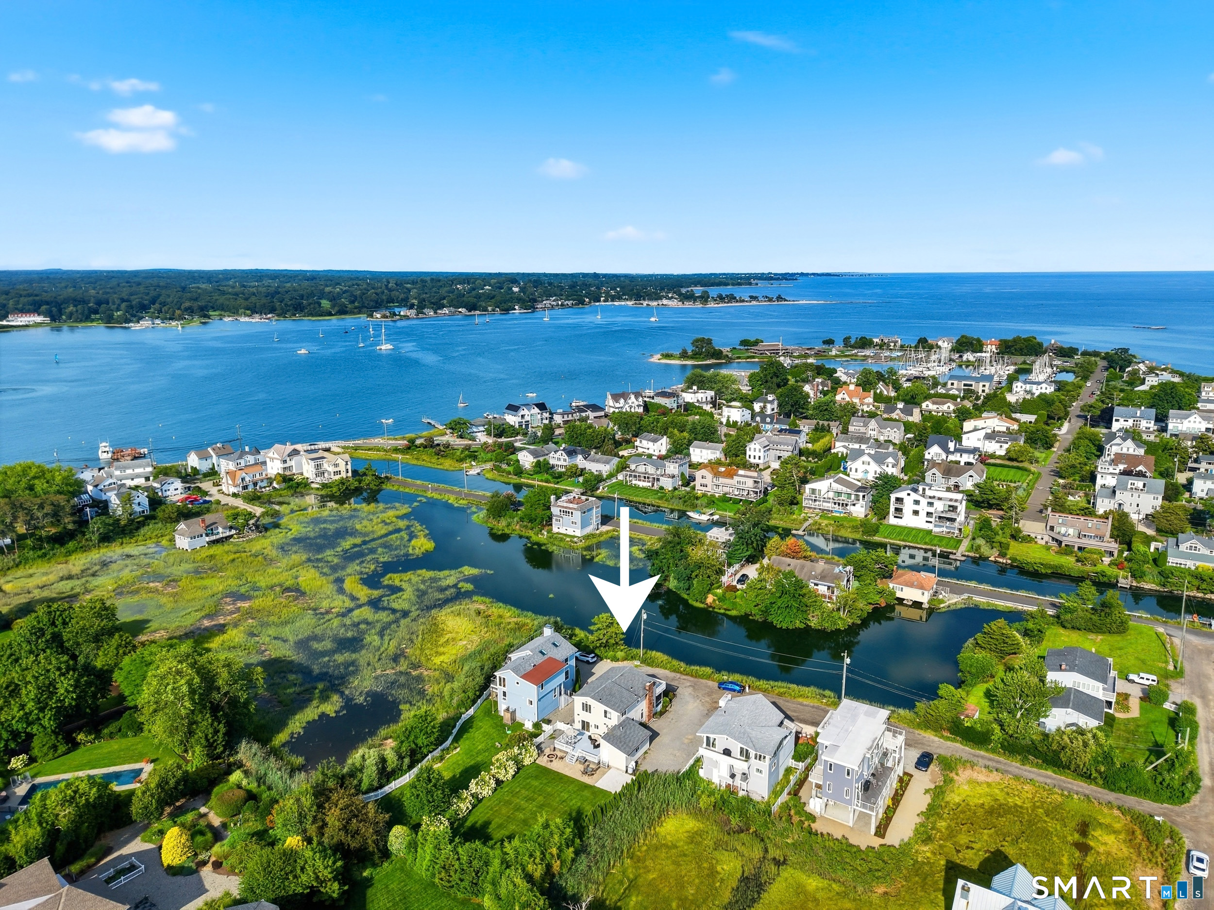 Aerial coastal neighborhood with an arrow indicating a waterfront home beside marsh and inlet.