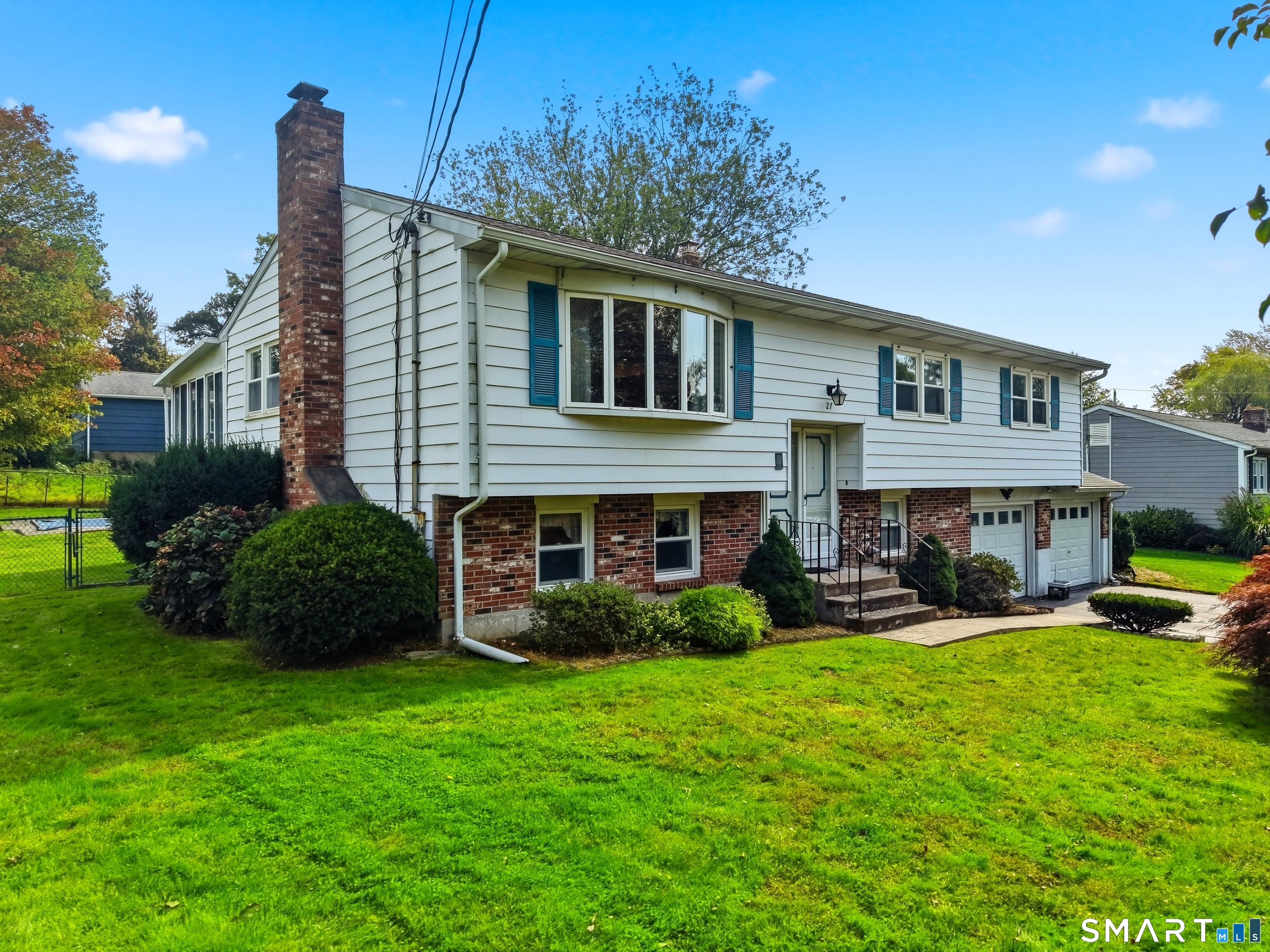 Split-level house with white siding, brick lower level, blue shutters, and a broad green lawn.