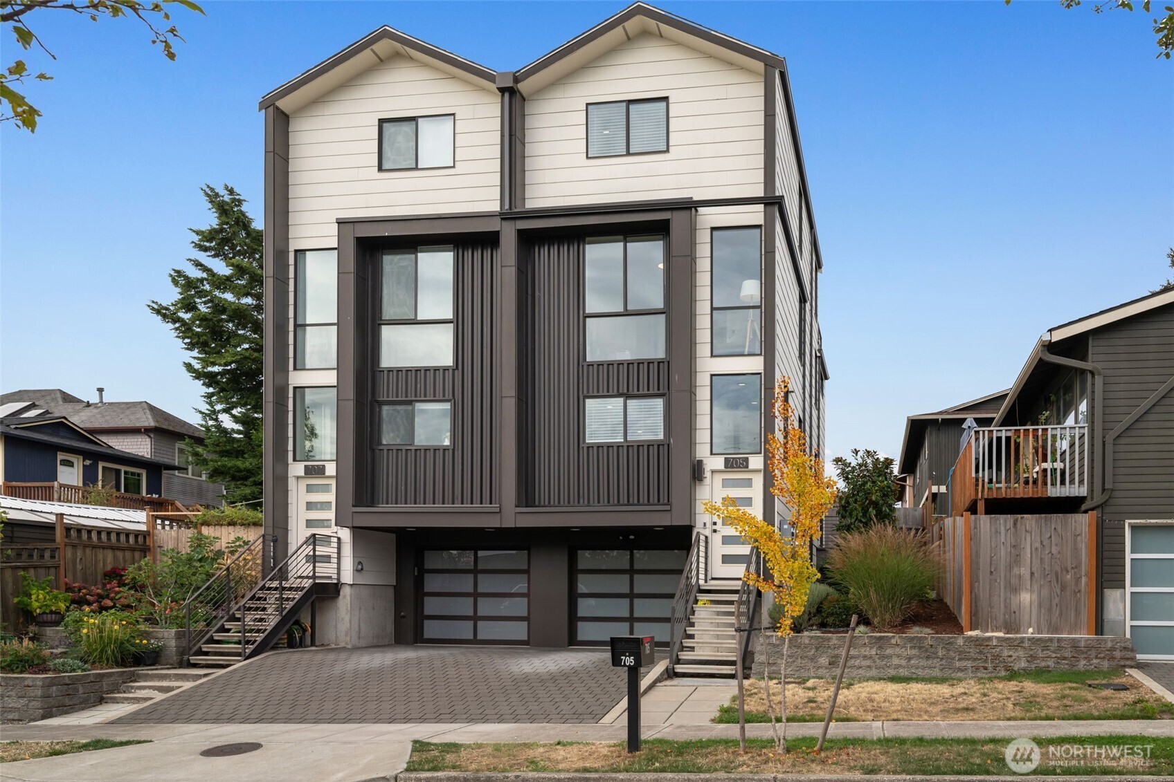 Contemporary multi-unit home with twin gables, dark facade panels, separate entries, and a paved driveway.