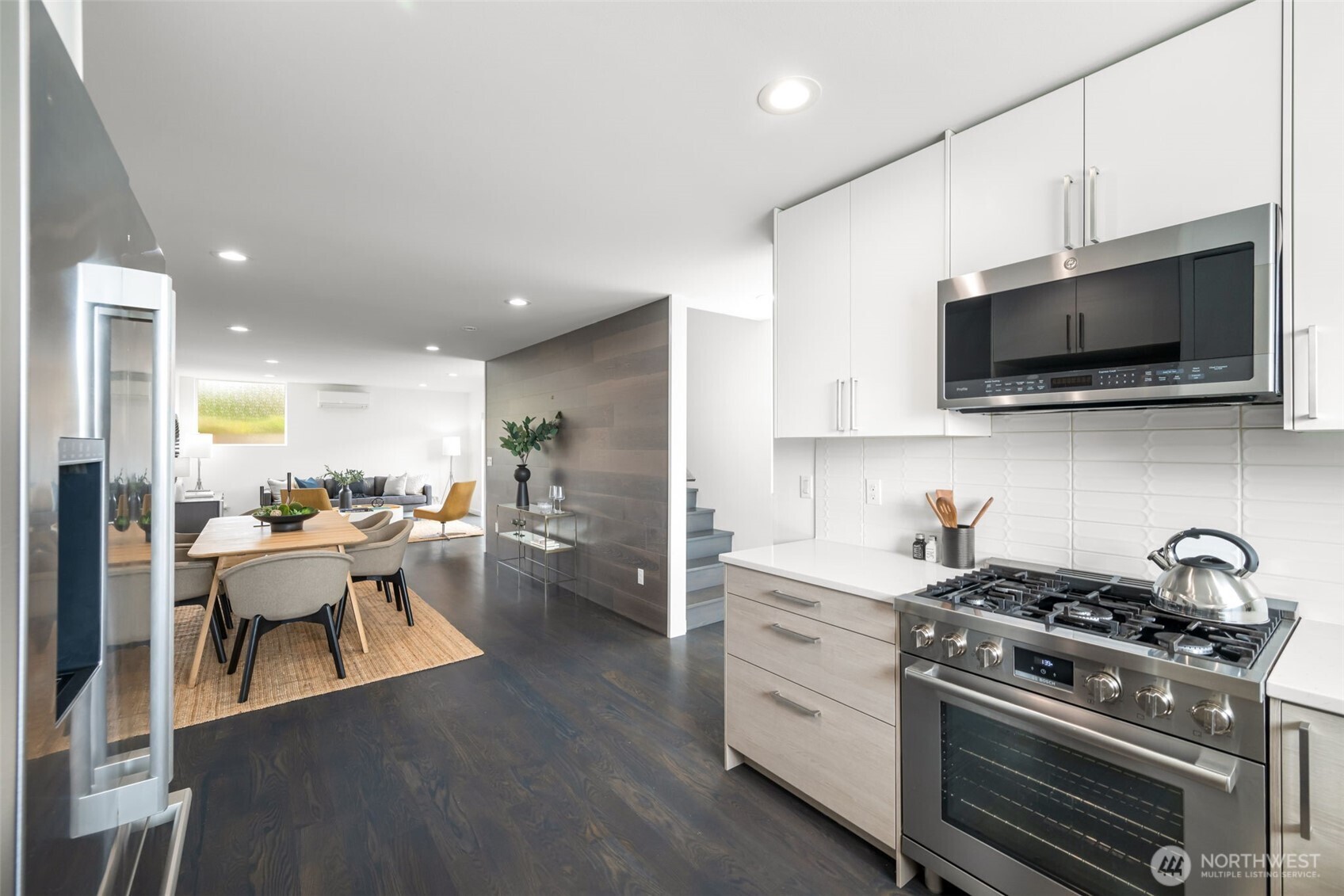 Modern kitchen with stainless steel appliances opening onto a furnished dining and living area.