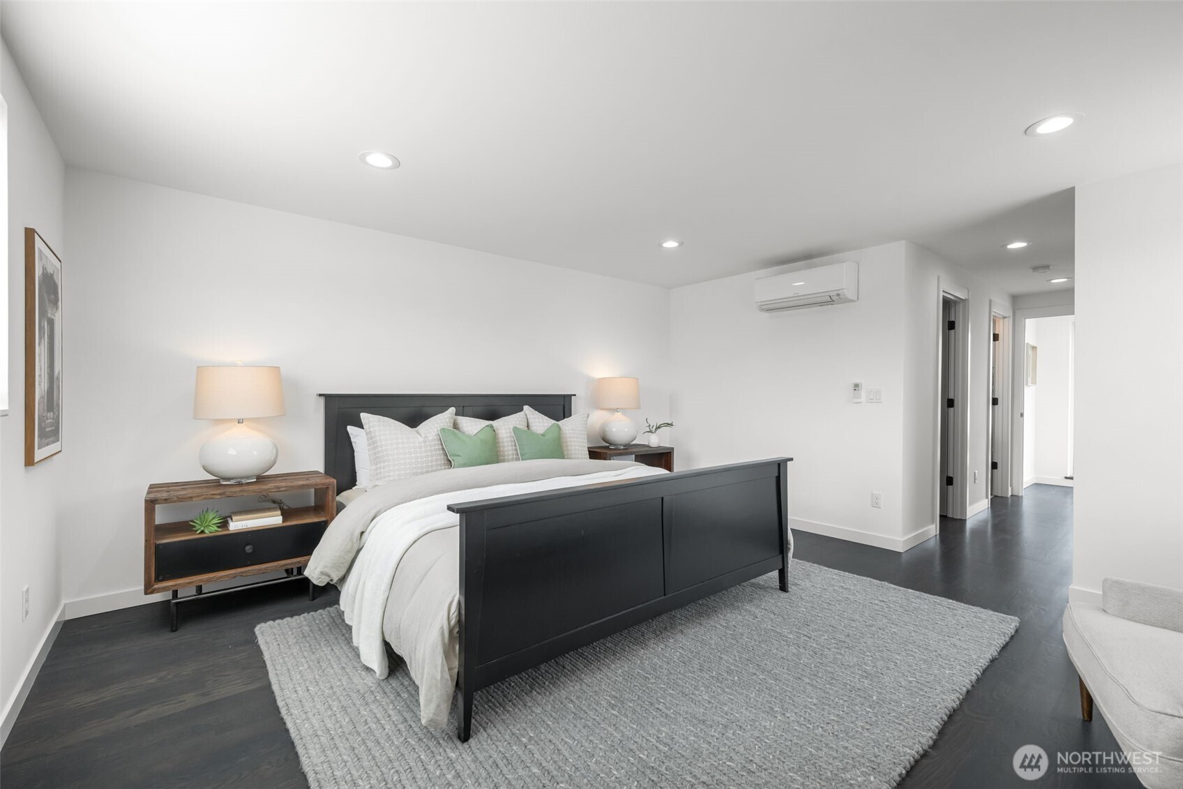 Staged bedroom with a black platform bed, white bedding, green pillows, and a large gray rug.
