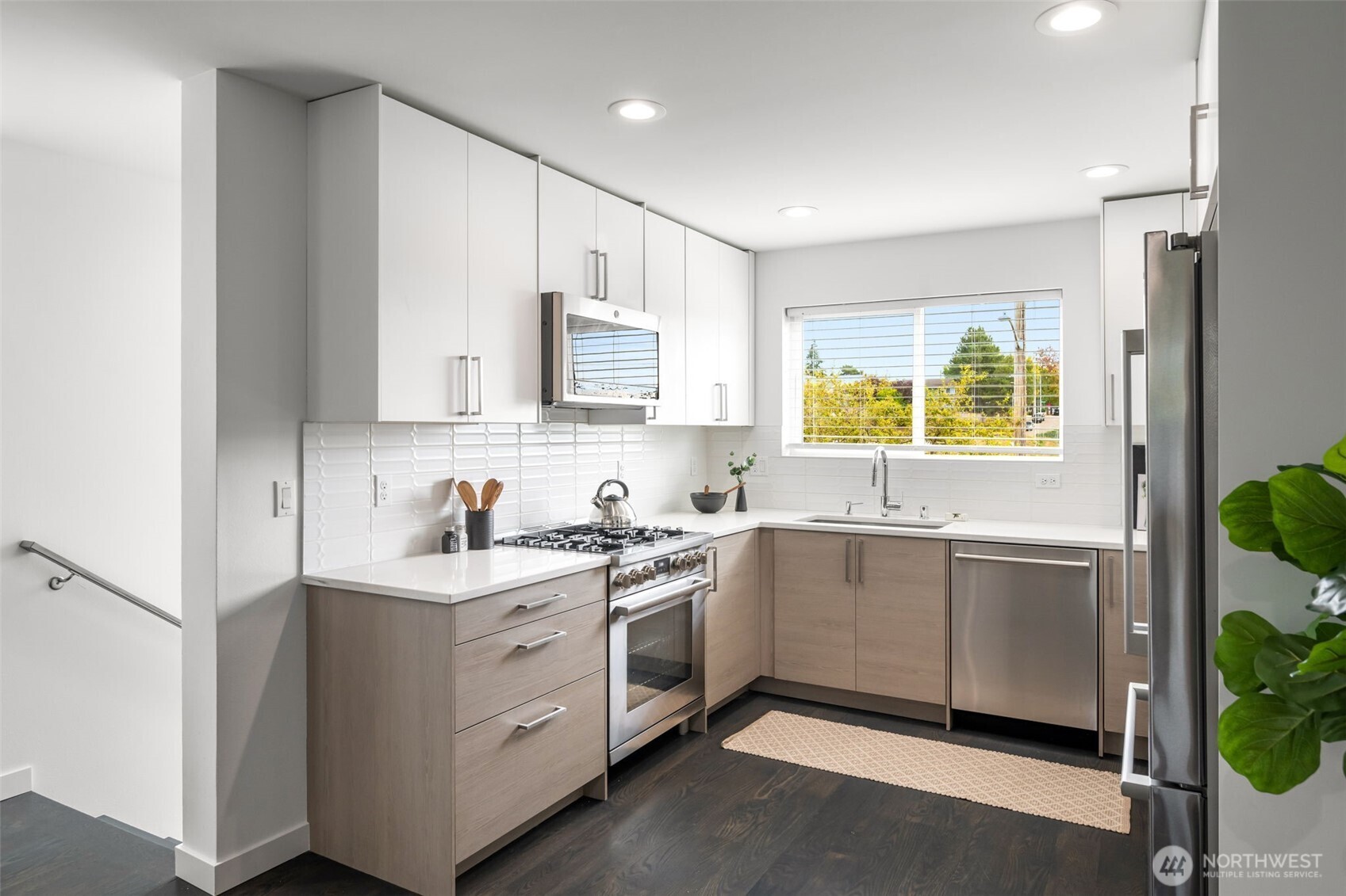 Bright modern kitchen with white cabinets, gas range, stainless appliances, and a window overlooking trees.