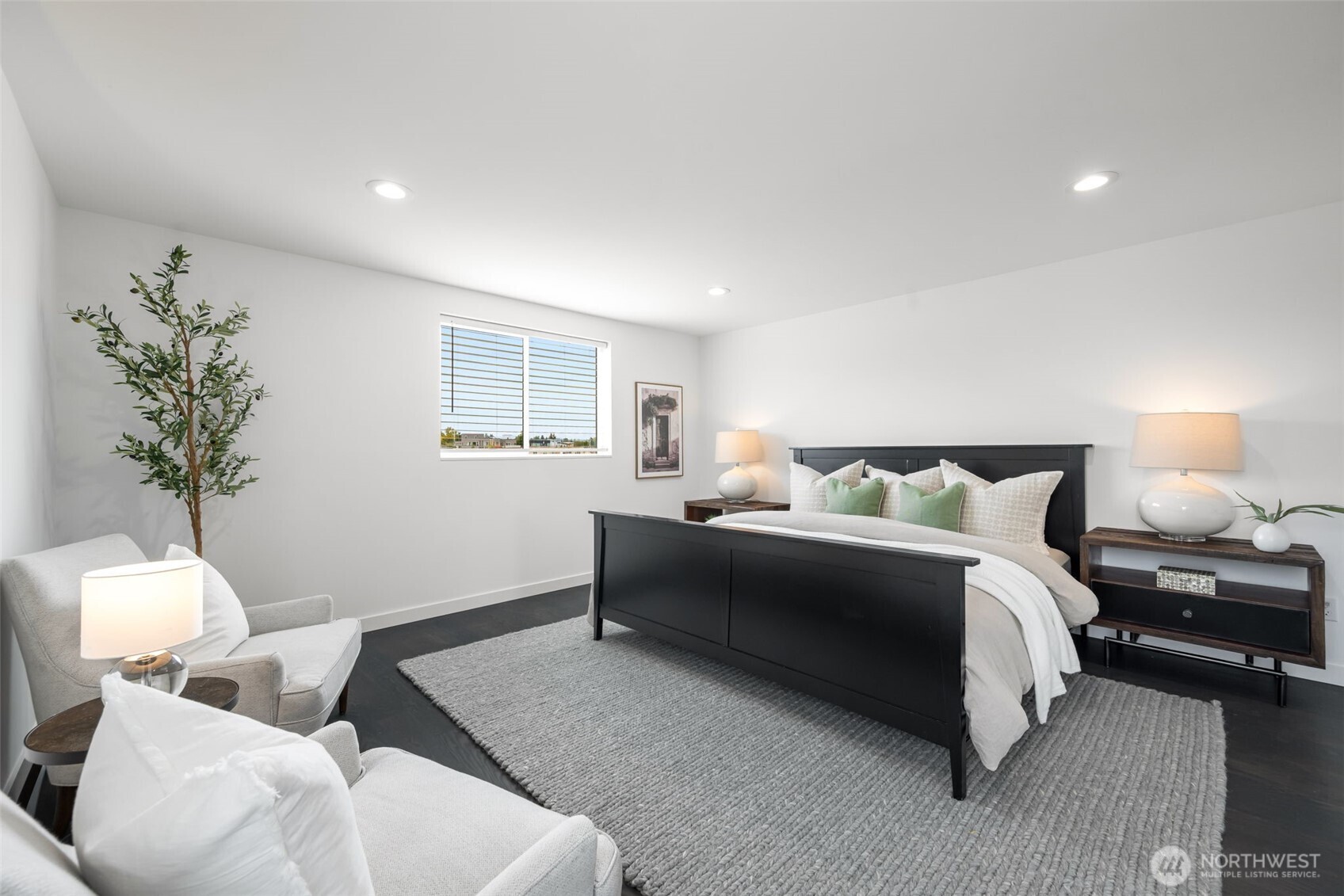 Staged bedroom with a black bed, green accent pillows, gray rug, and upholstered chairs.