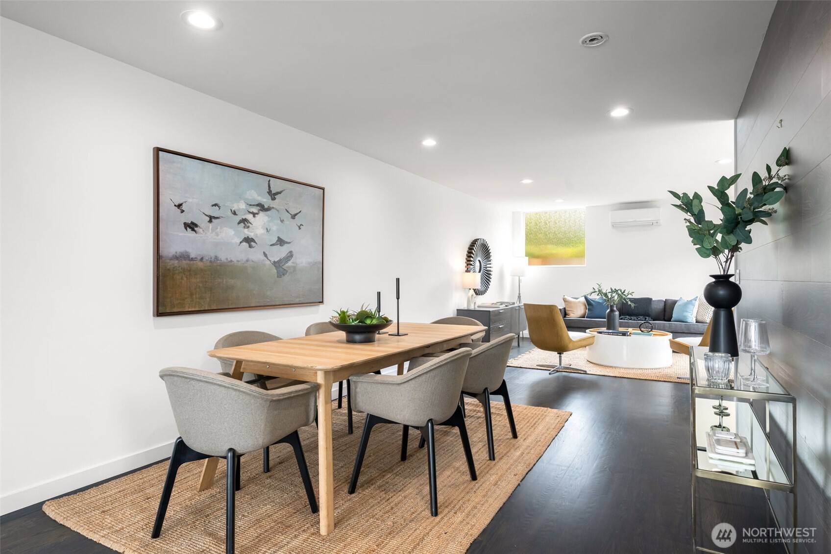 Open-plan dining and living room with a wood table, woven rugs, and a gray sofa.