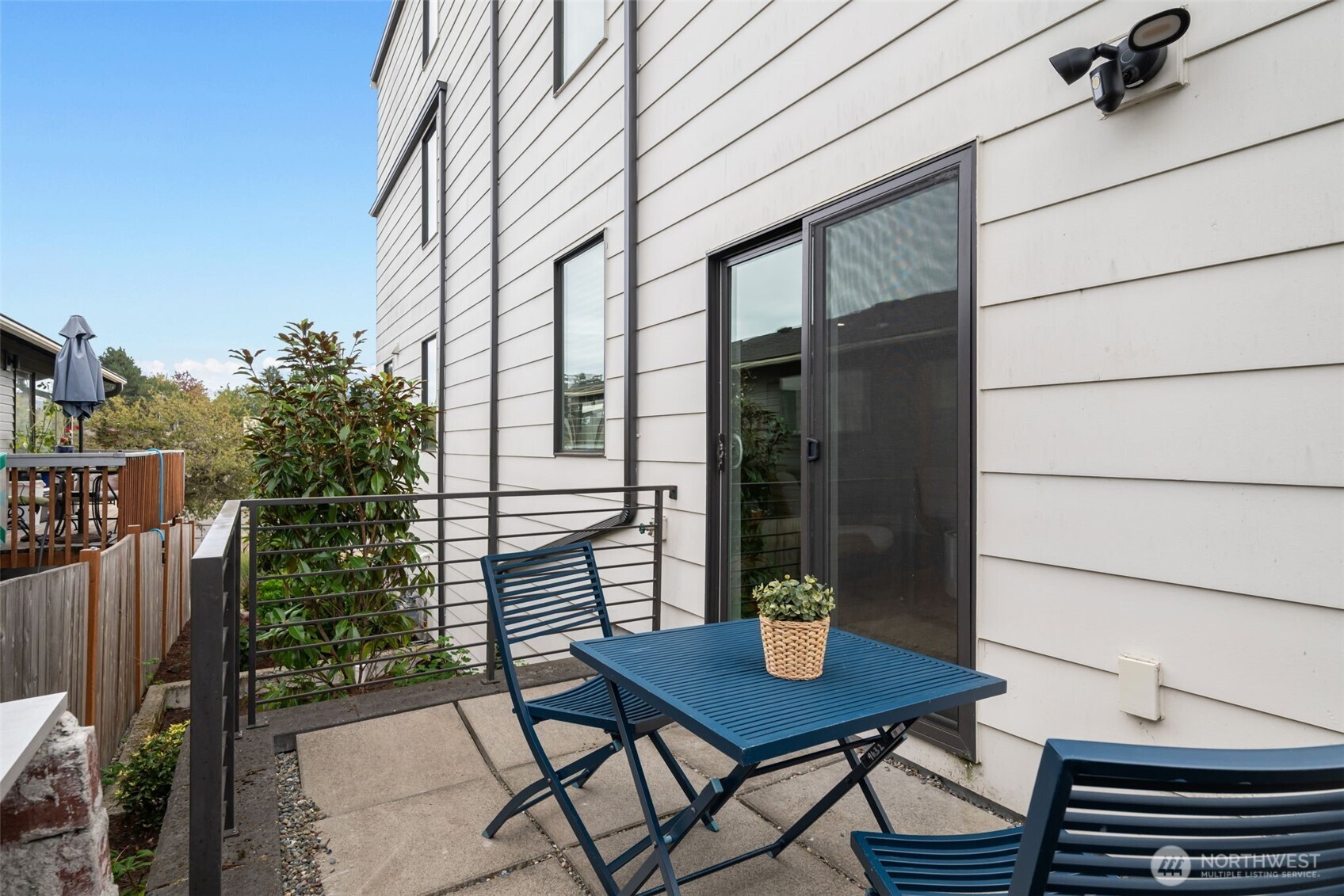 Outdoor patio with blue metal table and chairs beside a white-sided home.