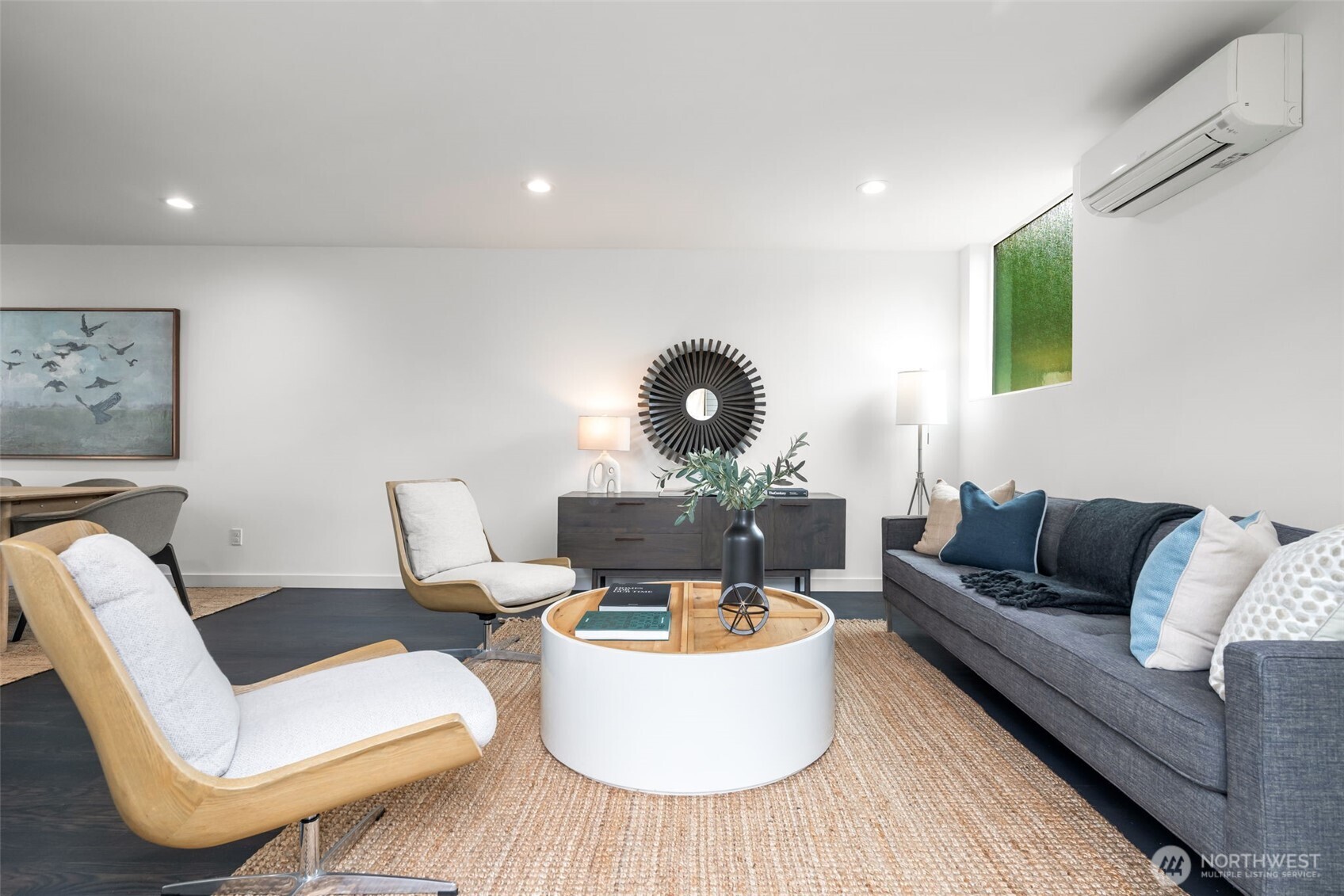 Furnished living room with a gray sofa, wood-framed lounge chairs, and a round coffee table.