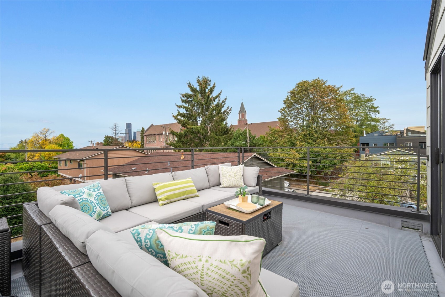 Rooftop deck with a gray sectional and city views beyond the metal railing.