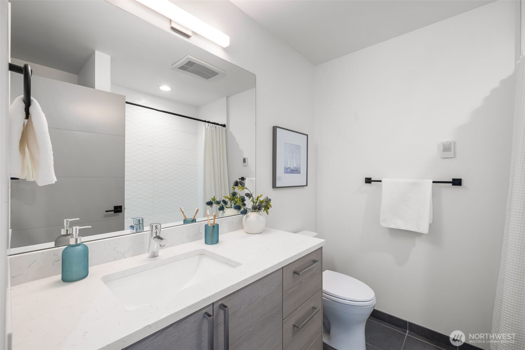 Modern bathroom with a wide mirror, white countertop, gray vanity, and dark tile floor.