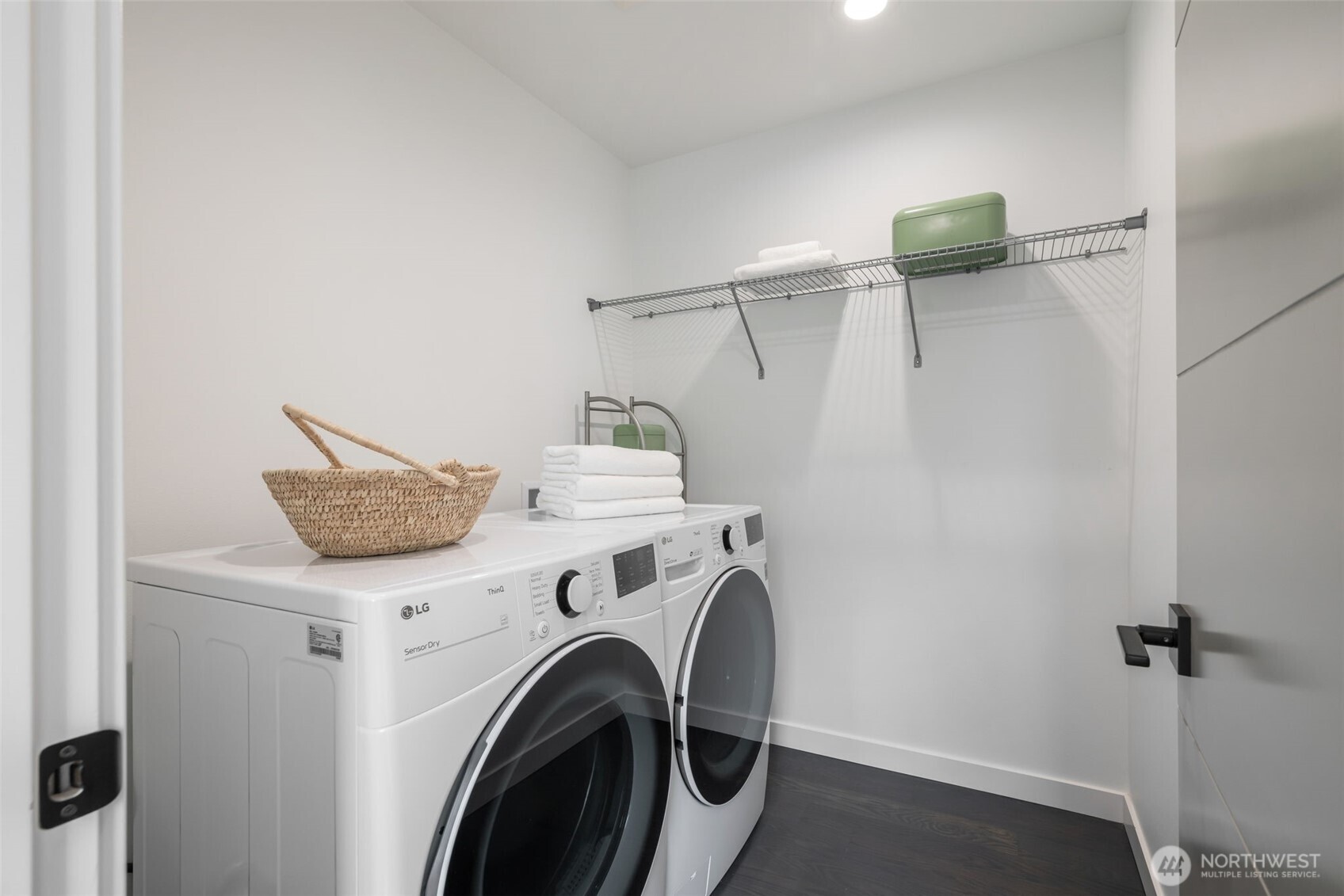 Laundry room with front-loading washer and dryer, wire shelving, folded towels, and a woven basket.