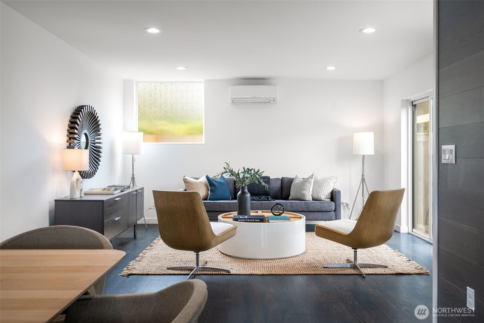 Staged living room with a gray sofa, wood lounge chairs, and a round white coffee table.