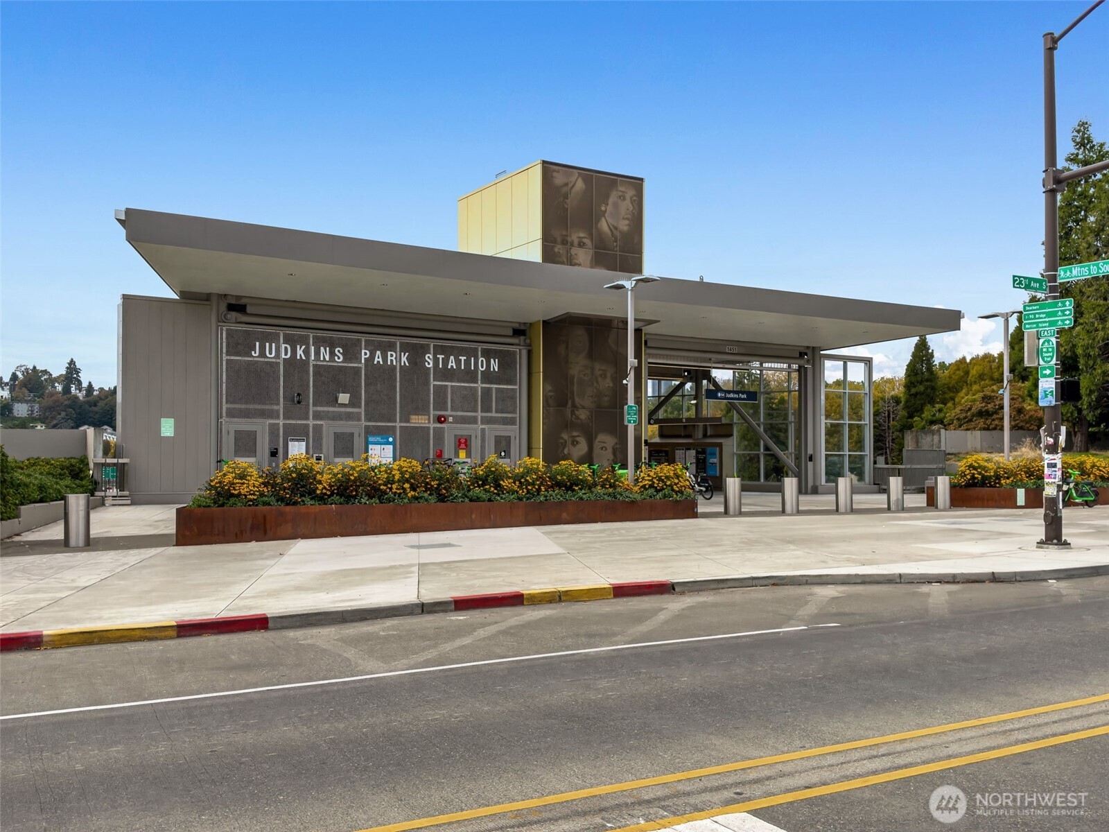 Judkins Park Station with a broad canopy, flower planters, and light rail tracks in the foreground.