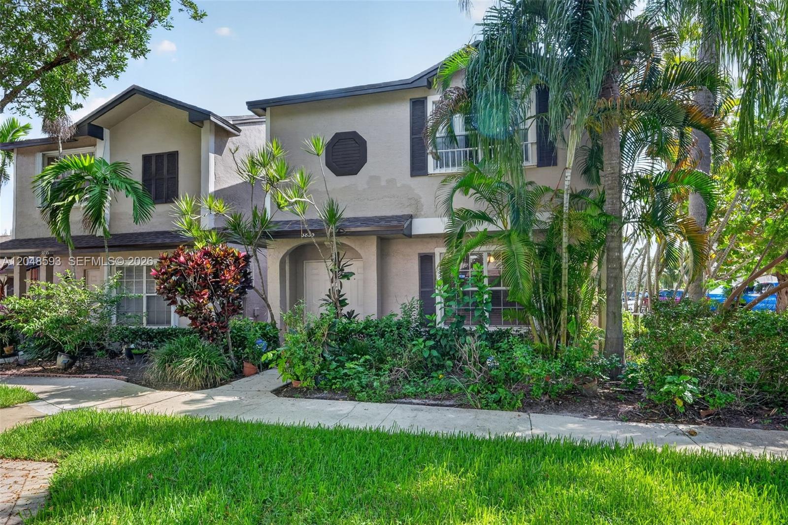 Two-story townhouse framed by palms and tropical landscaping.