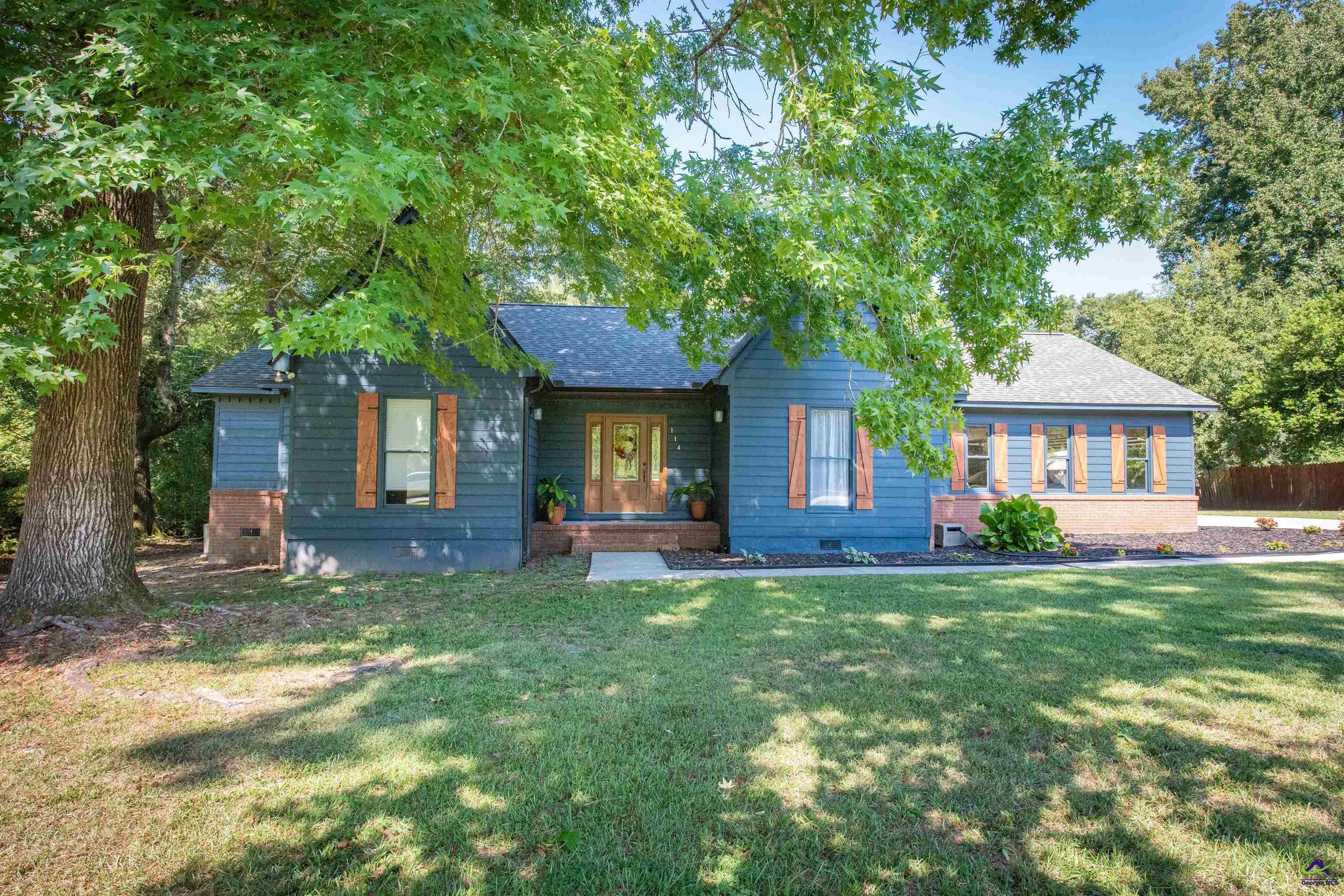 Blue single-story home with wood shutters and a shaded front lawn beneath mature trees.