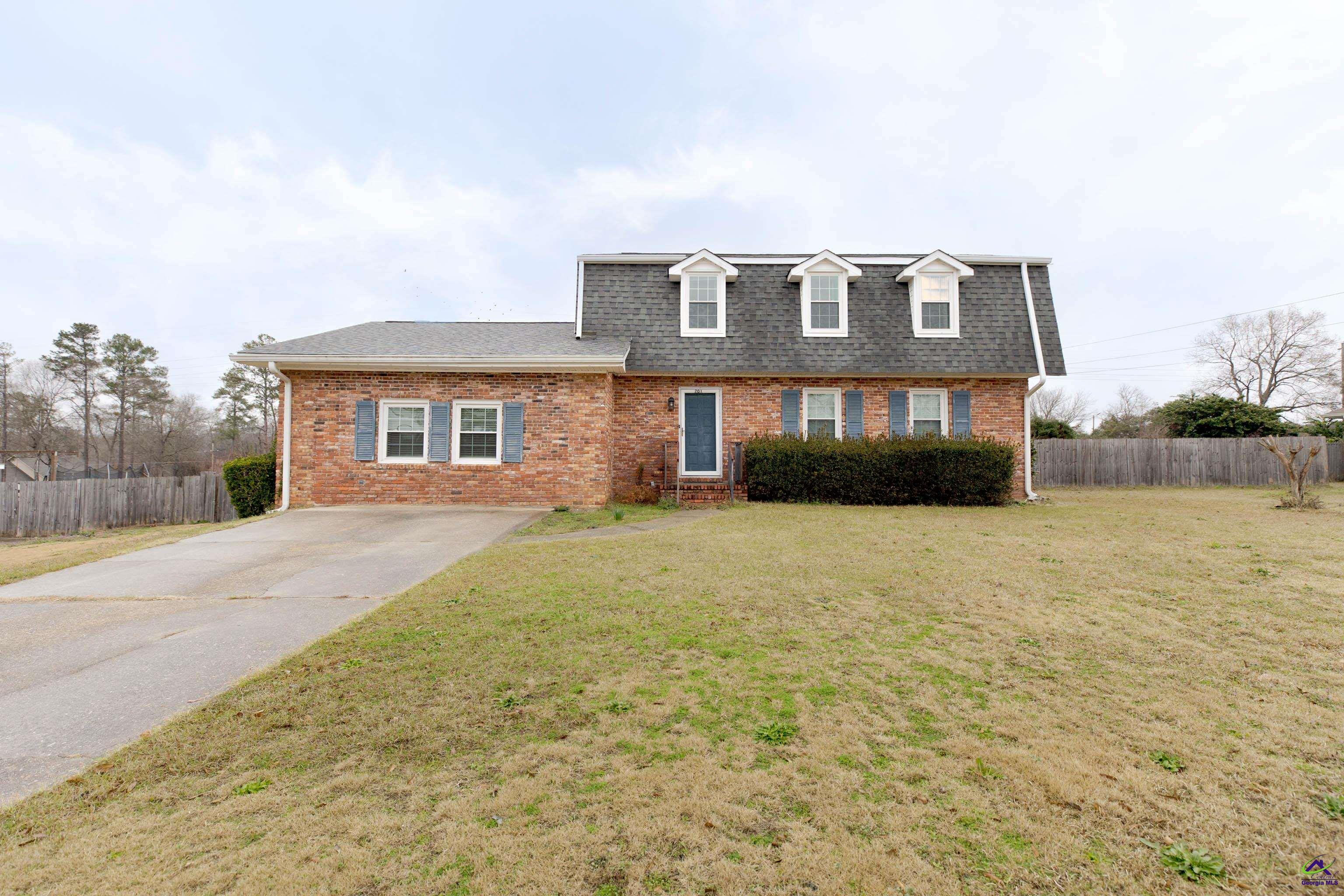 Red-brick two-story home with three roof dormers, blue shutters, a driveway, and a fenced yard.
