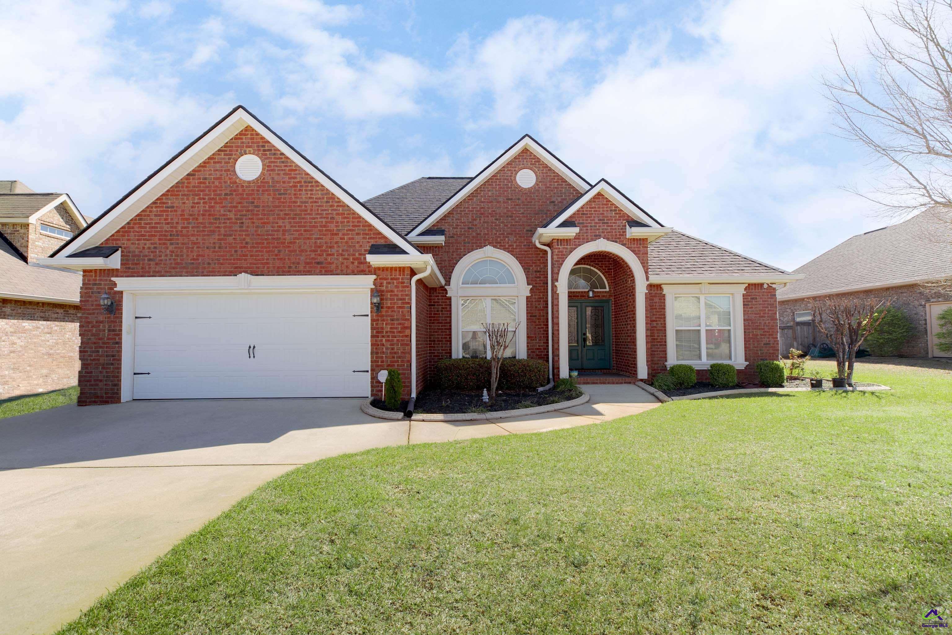 Red-brick home with a white garage, arched entry, and broad green front lawn.