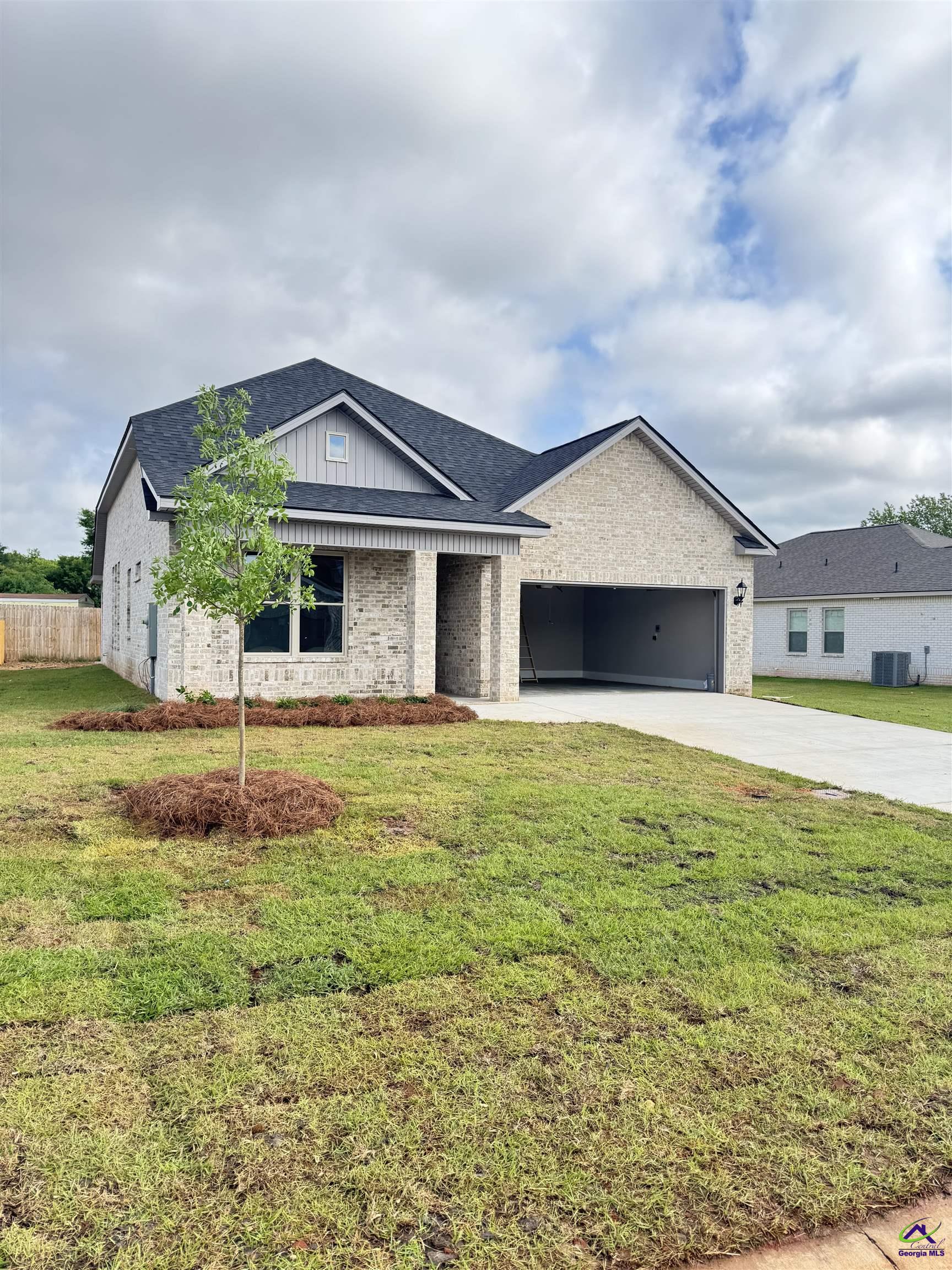 Brick house with an attached garage, broad driveway, and young tree in the front lawn.