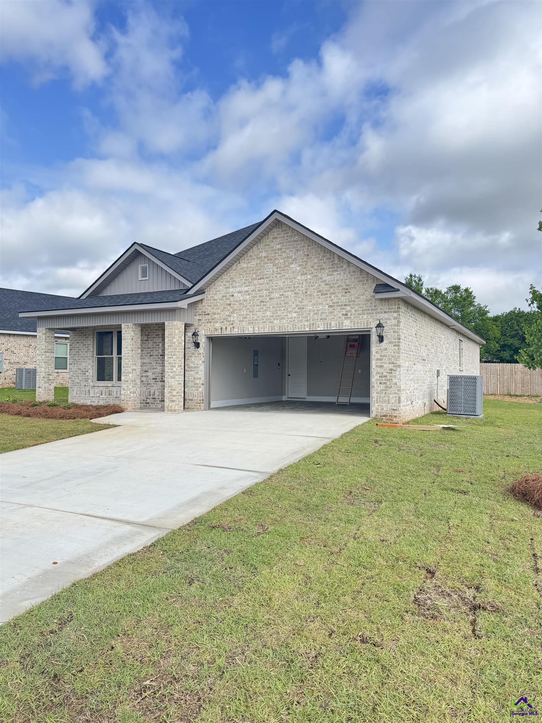 Light brick house with a dark gabled roof, open garage, and broad concrete driveway.