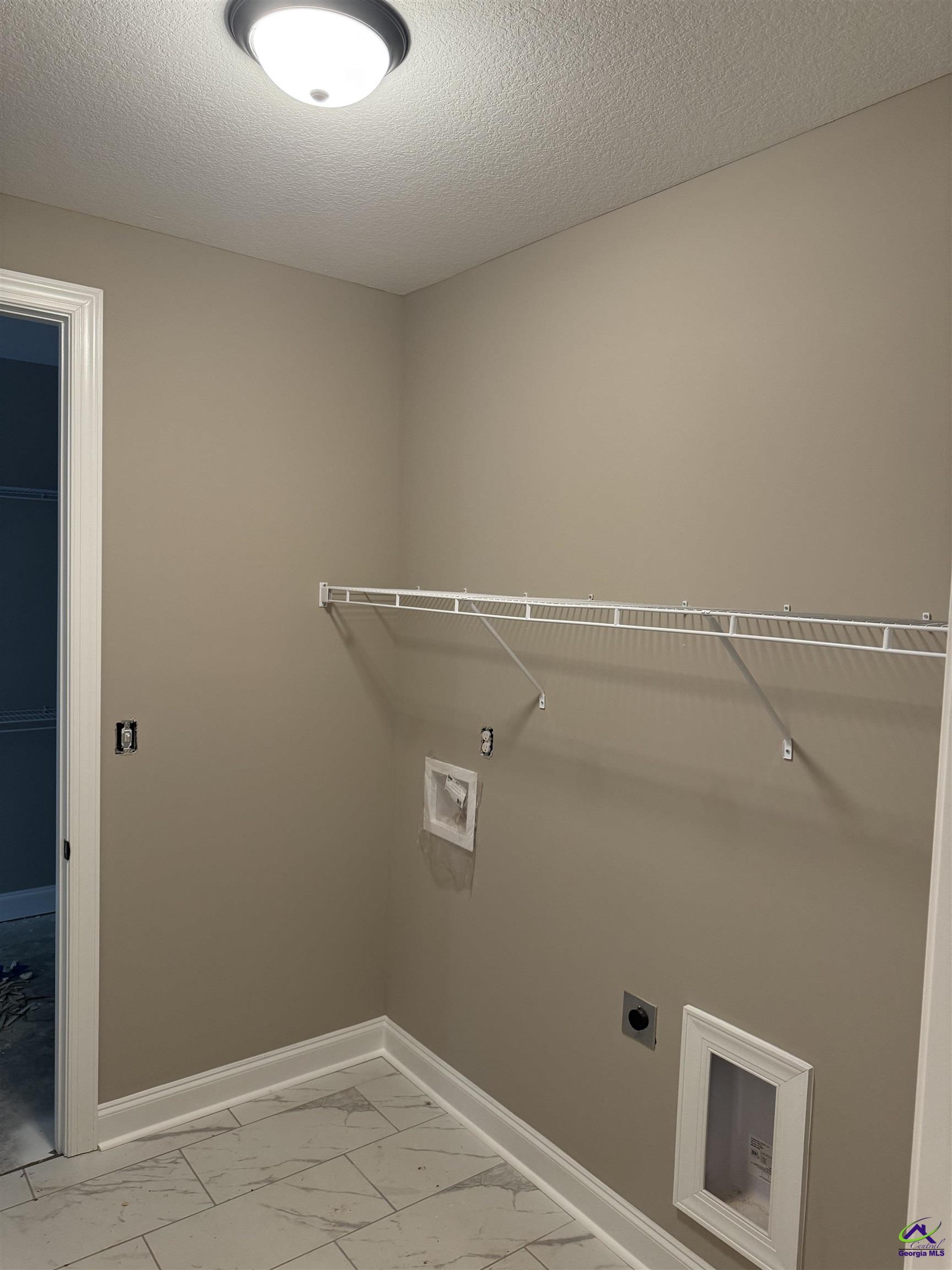 Empty laundry room with a long wire shelf, marble-look tile floor, and a small pet door.