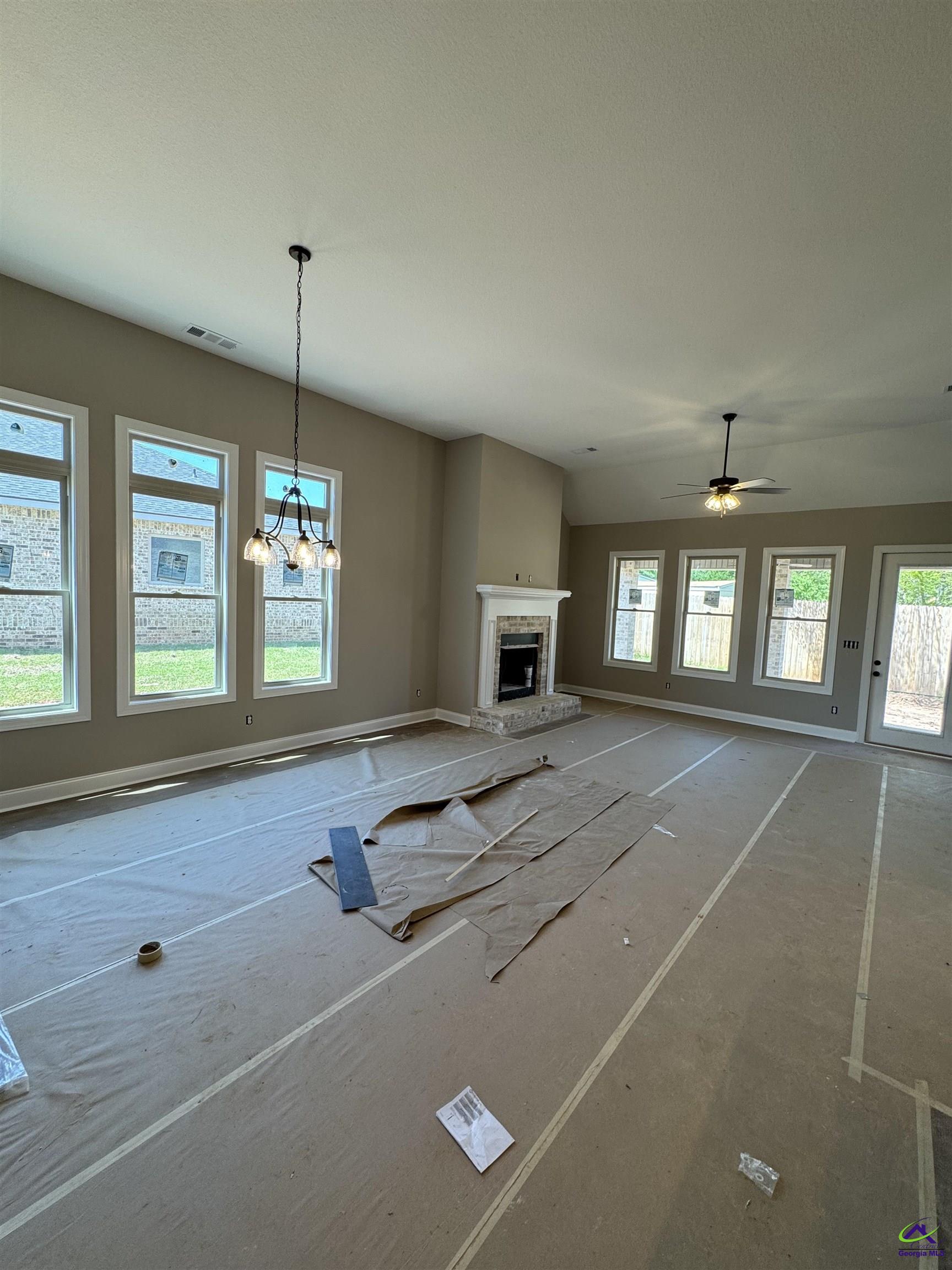 Unfinished living room with a stone fireplace, tall windows, and protective floor covering.