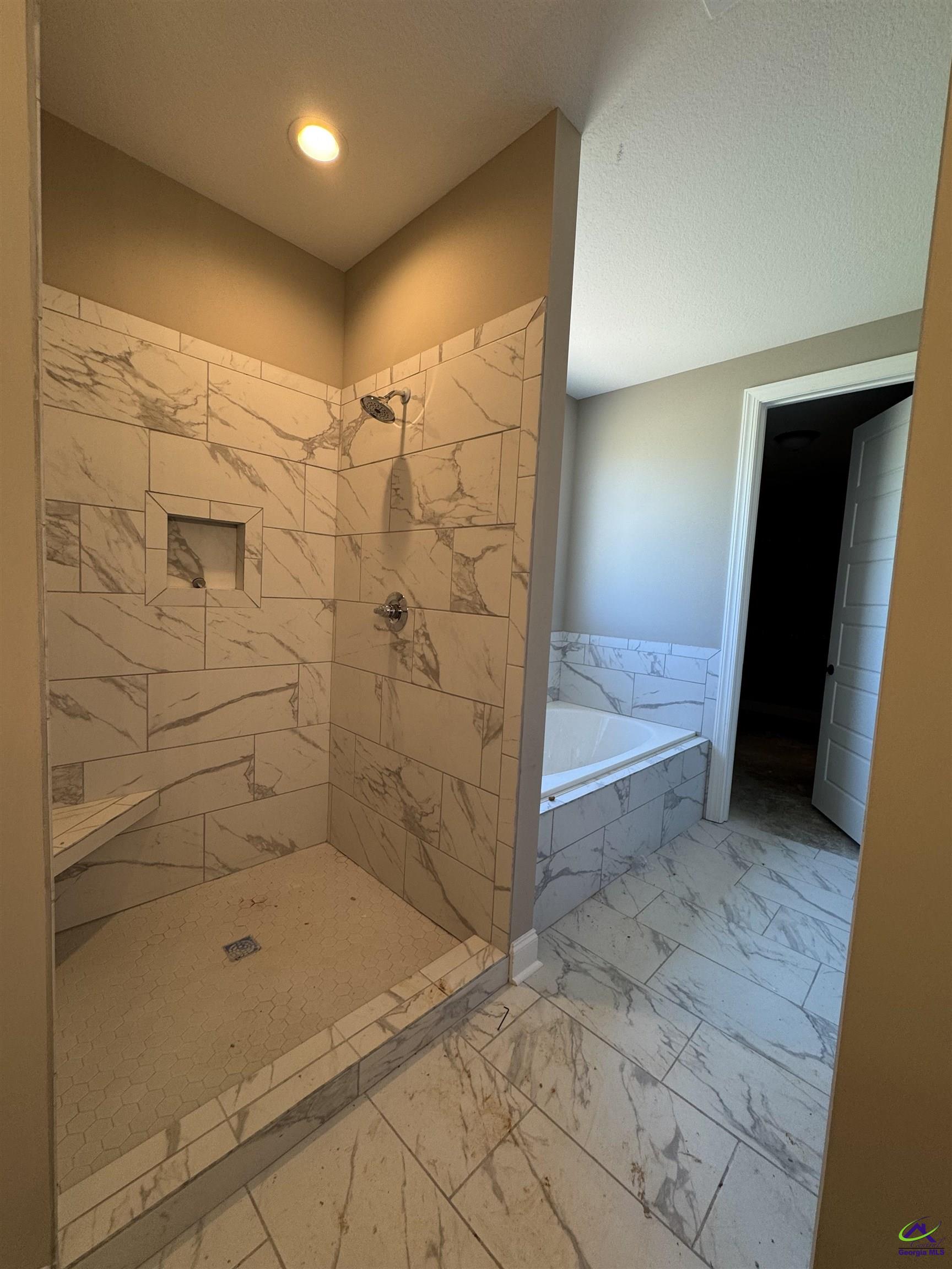 Bathroom with a marble-look tiled walk-in shower and matching bathtub surround.