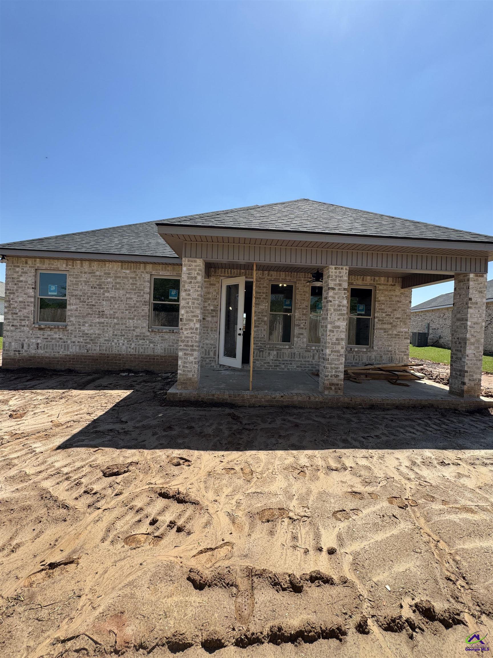 Brick home under construction with a covered rear patio and unfinished yard.